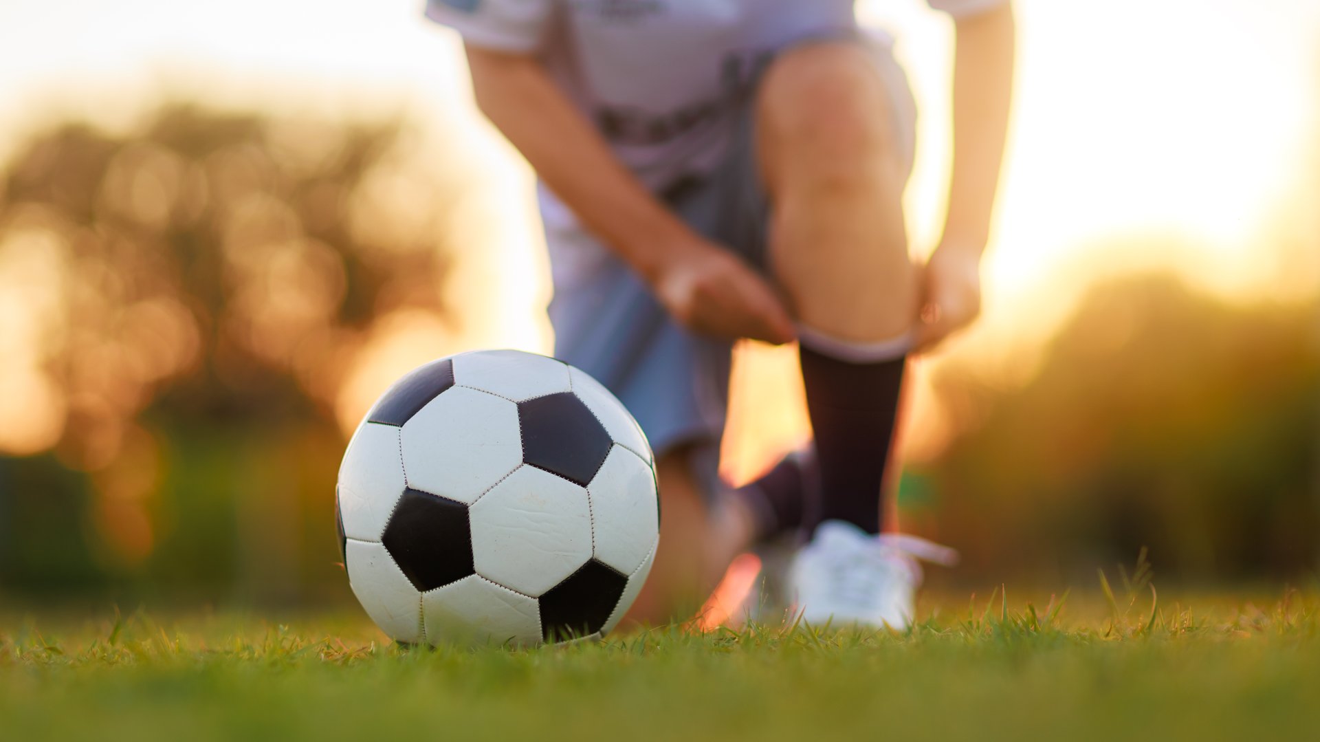 Soccer player with a ball. Action sport outdoors playing football for exercise at green grass field under the twilight sunset. Picture with copy space.