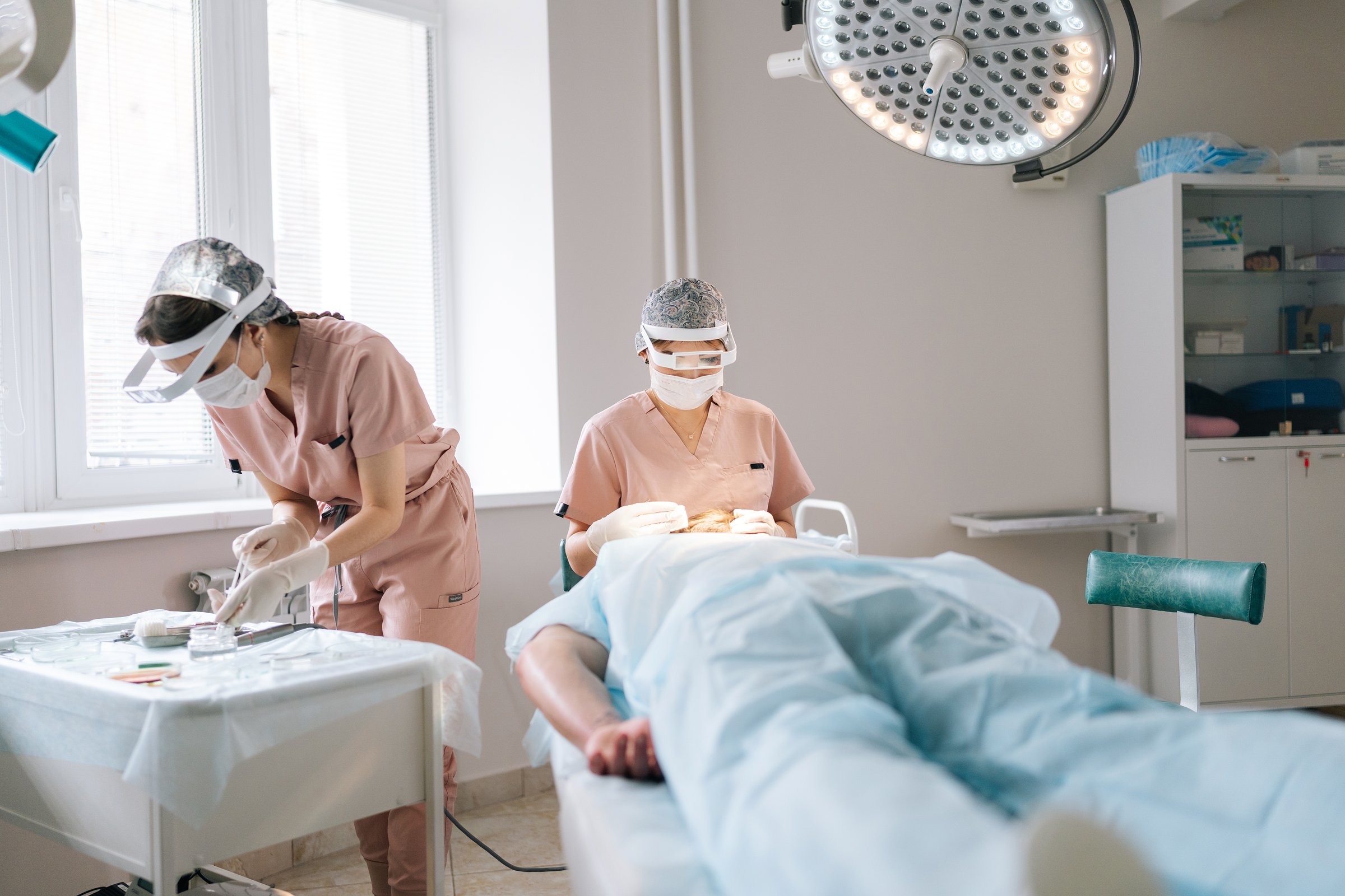 Female dermatologist performing local anesthesia to back of head in recipient area prior to hair transplant surgery. Male patient receiving hair loss treatment injections in scalp by trichologist .