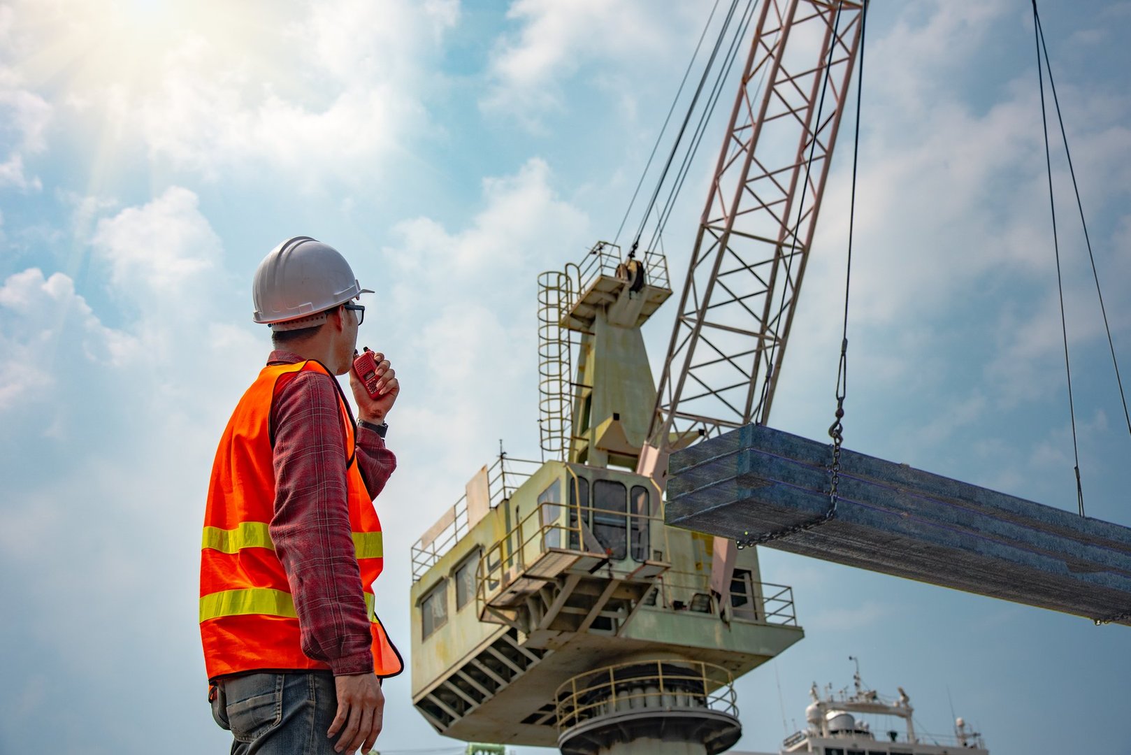 worker stevedore or foreman, engineering, loading master talks to crane driver by walkie talkie for safety lifting the goods shipment, lifting by gantry crane, working at risk on the high level insurance