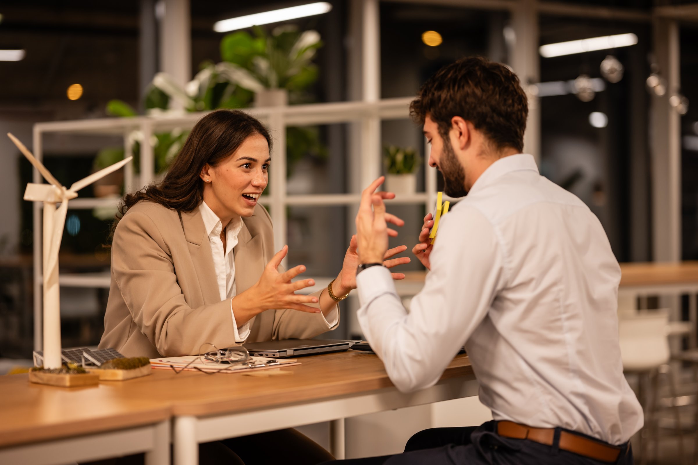 Business partners engaging in a lively conversation, planning sustainable energy solutions with a desk model of a wind turbine