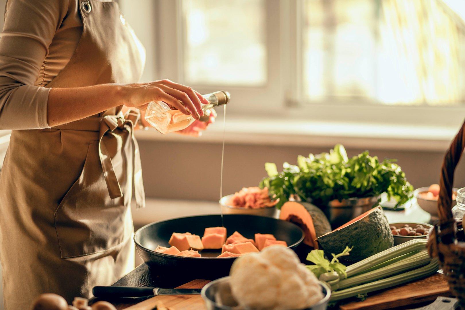 Hands of young woman put pumpkin on frying pan for baking in the kitchen. The concept of healthy eating