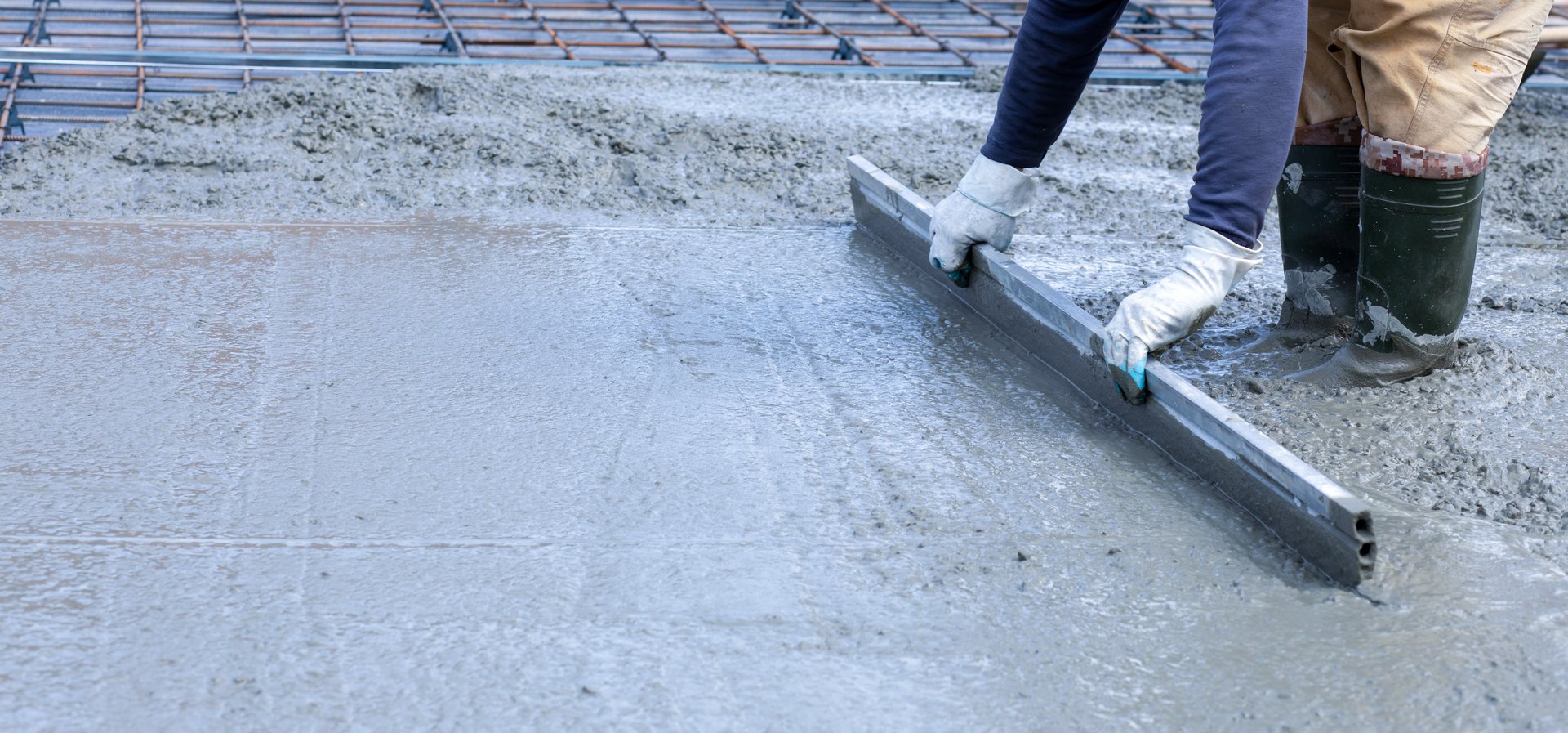 The concept of concrete leveling. A worker levels concrete using a surface rule.