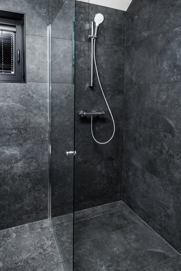 Sleek walk-in shower with chrome fixtures, glass partition, and dark grey tiles, offering a modern and elegant bathroom design with minimalist aesthetics