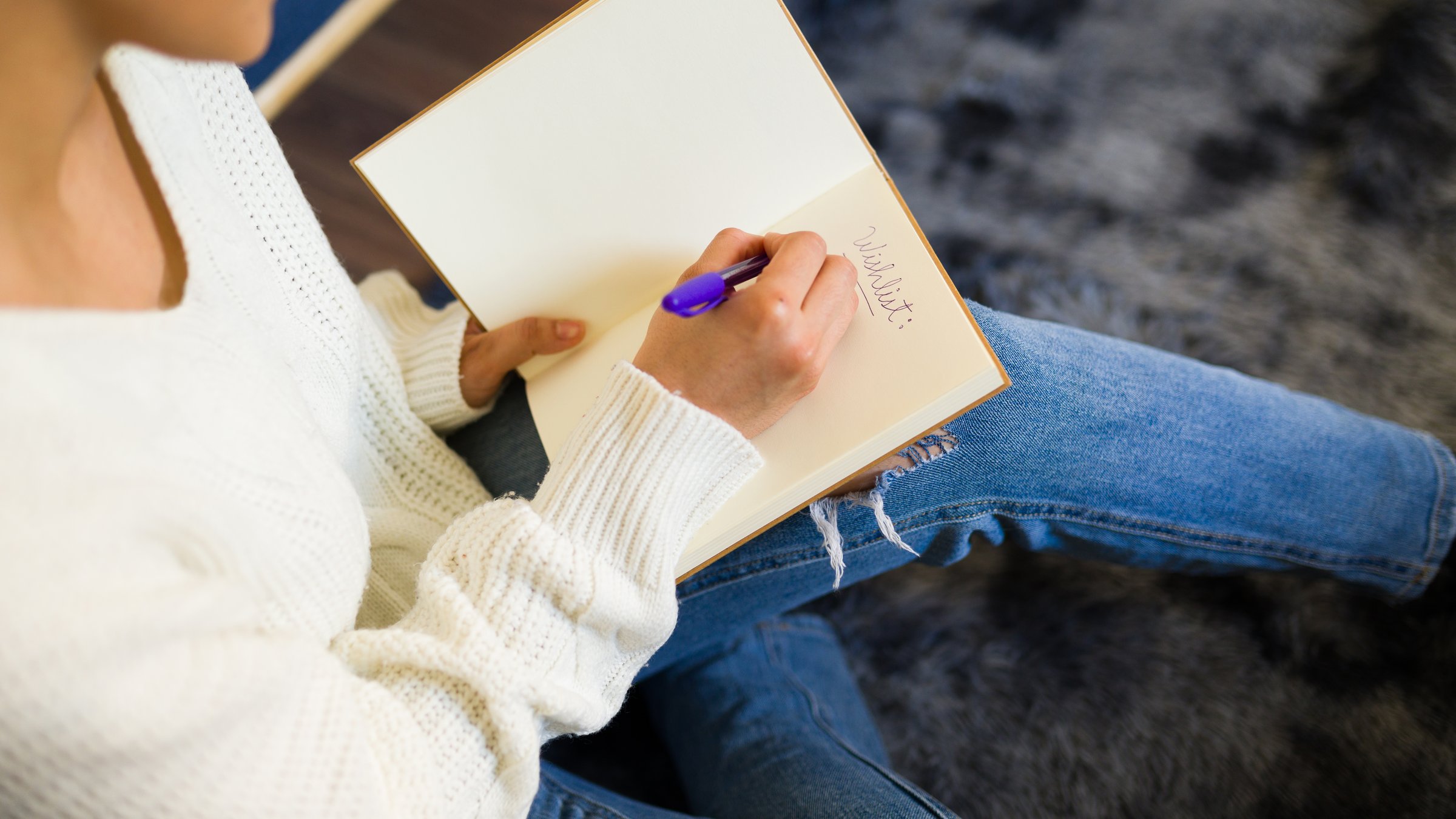 Woman is sitting comfortably at home writing her christmas wishlist in a notebook with a purple pen