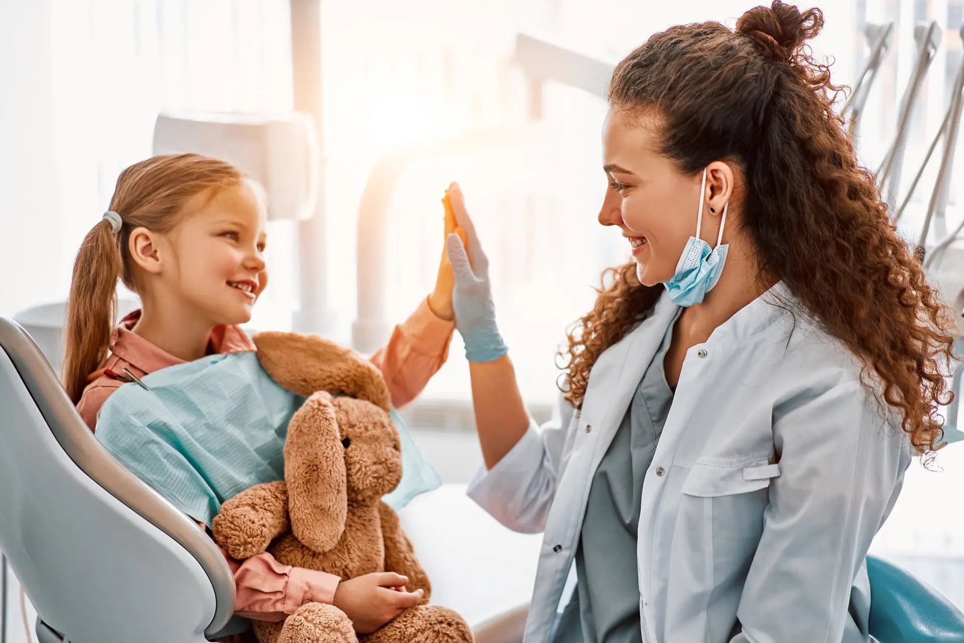 A cheerful patient in a dental chair smiles at a dentist during the appointment. The bright clinic features modern equipment.