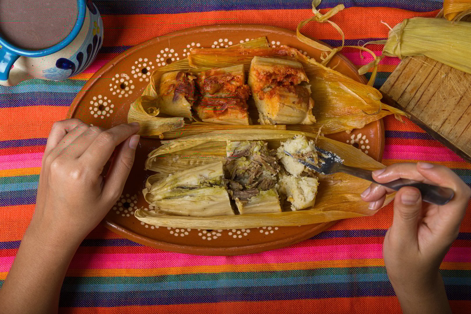 Hands of a person cutting a tamale with a fork. Tamale, typical Mexican food.
