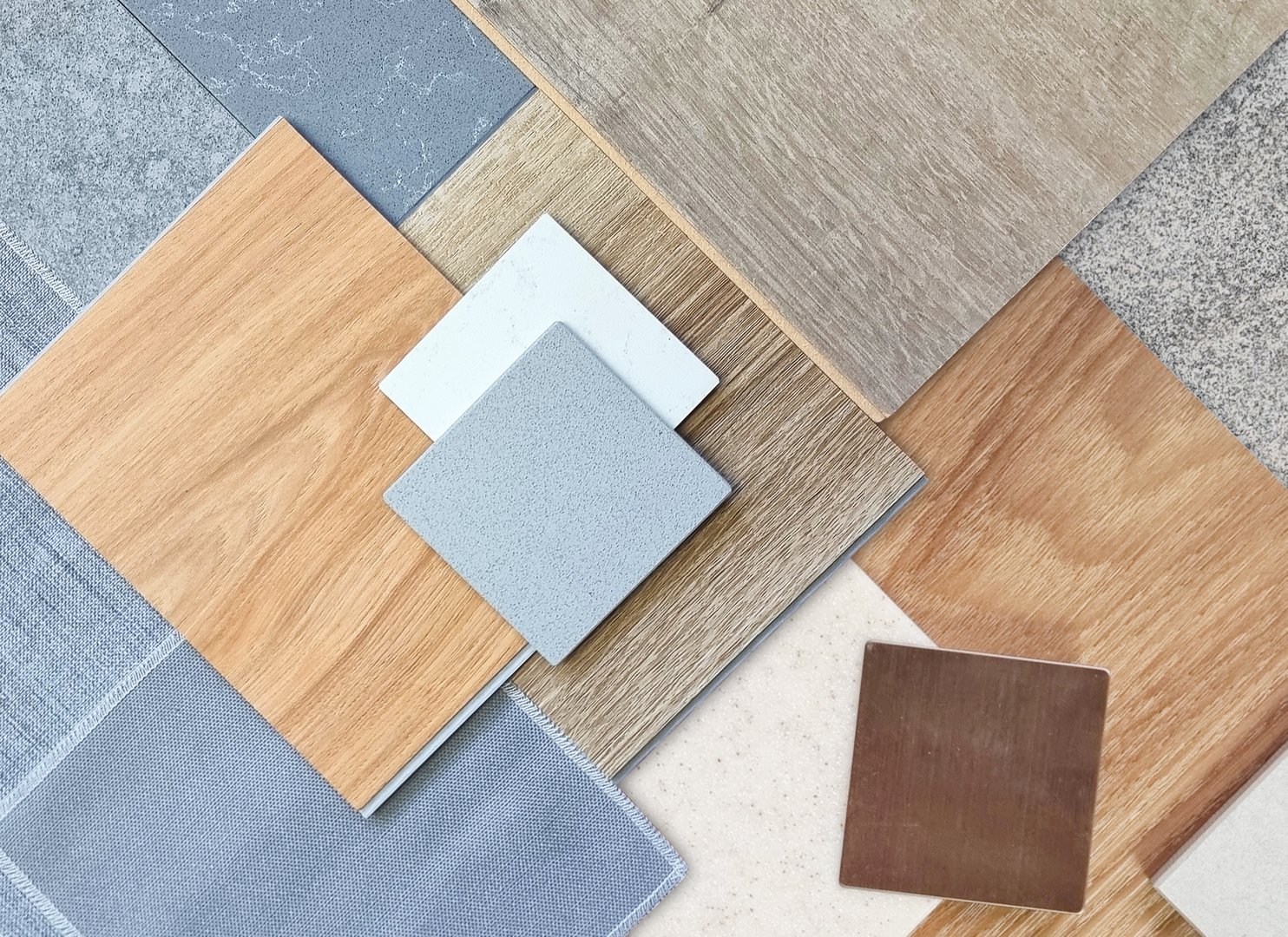 top view of interior material samples contains wooden laminate flooring tile, artificial stone, wooden vinyl flooring tile, quartz stone, grey fabric, gold brushed stainless, stone tile in top view.