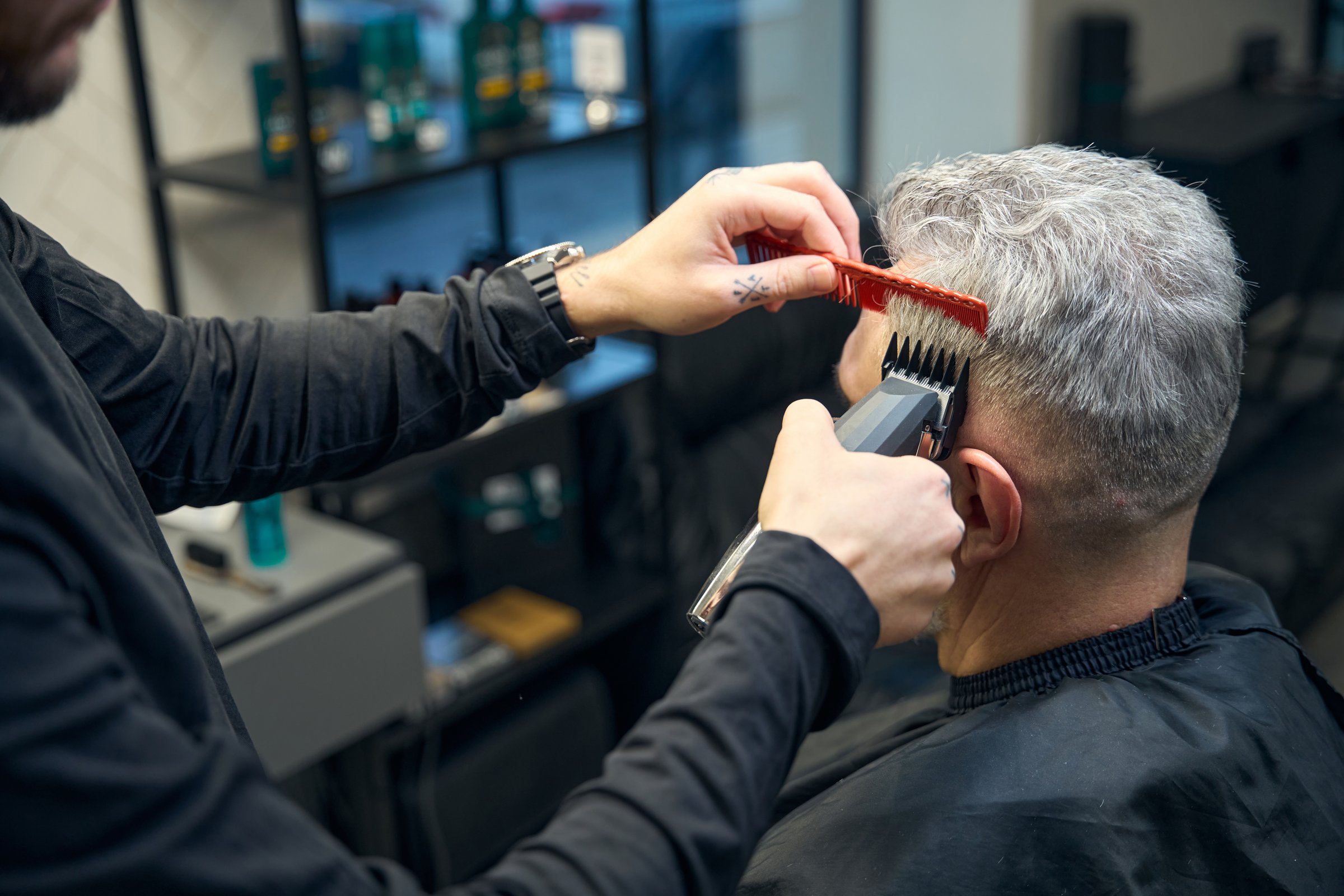 Portrait of hairdresser doing a machine haircut to adult man with gray hair. Haircut, customer service concept