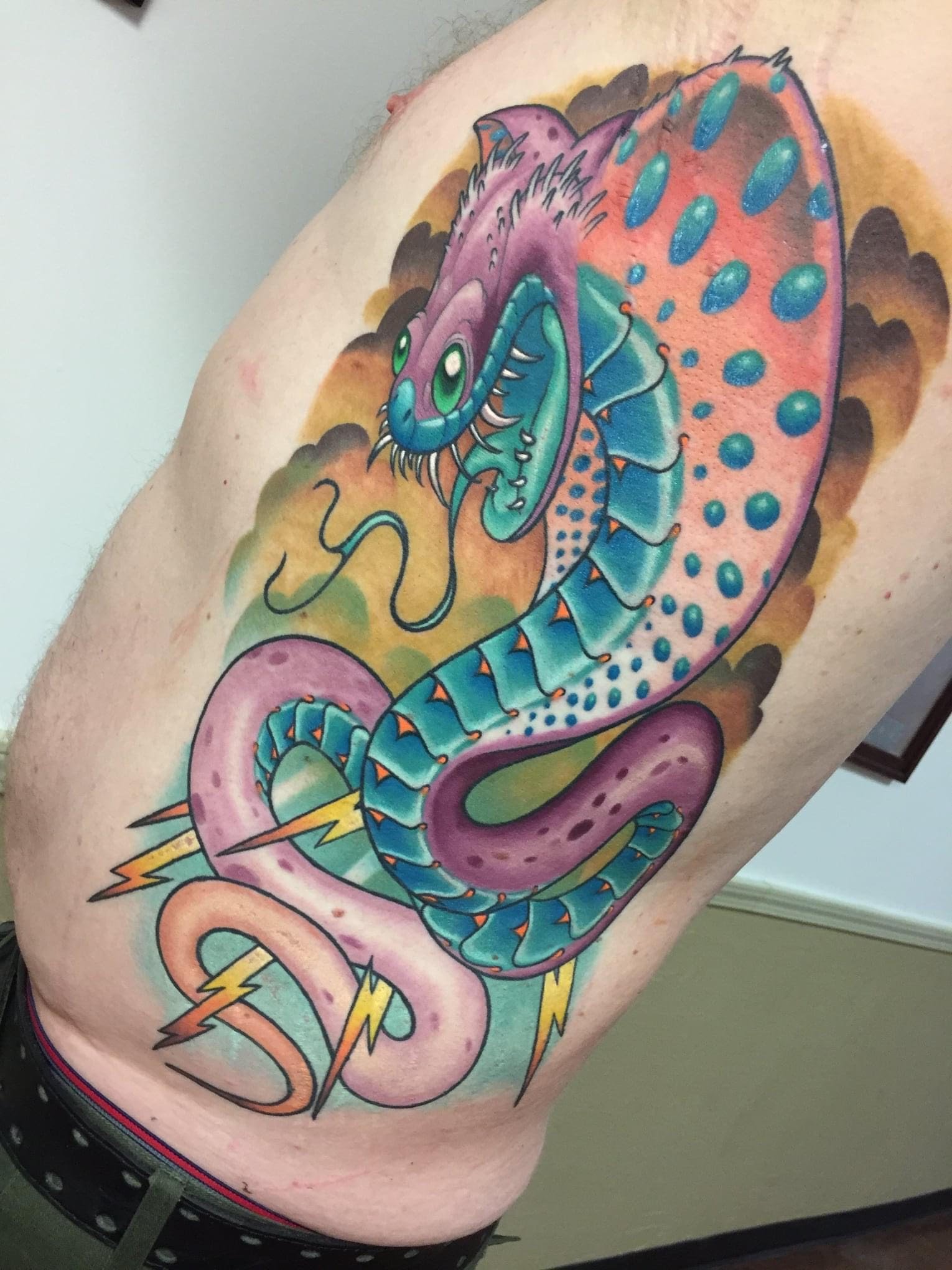 Colorful tattoo of a stylized snake with scales and lightning bolts on a persons back.