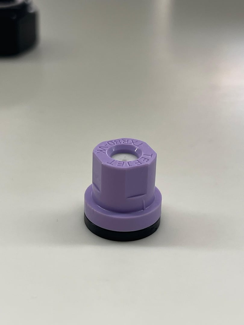 Purple hexagonal cap with a black base on a white surface, likely for sealing containers.