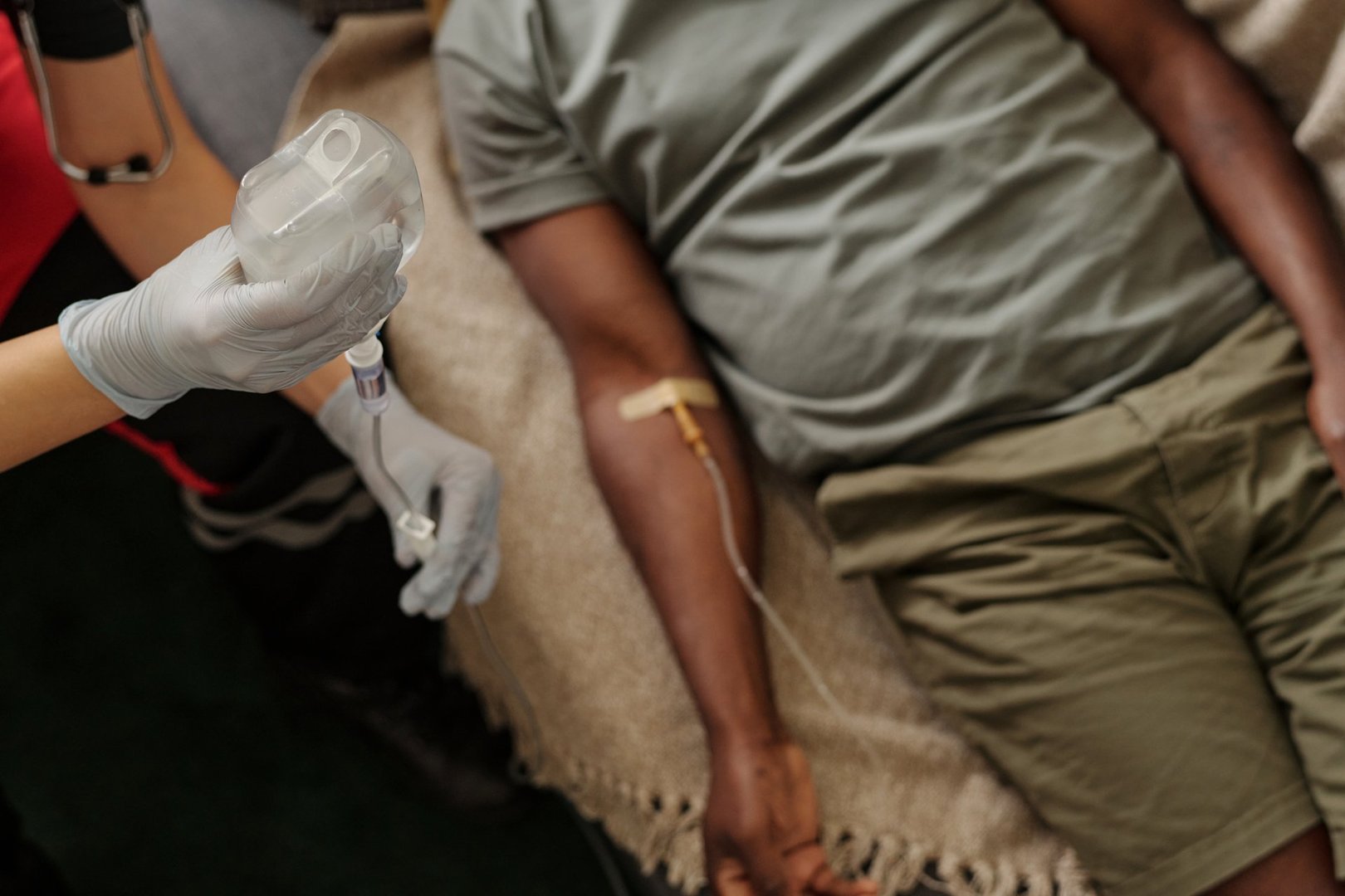 Medical professional holding IV bag while patient receives intravenous infusion lying on medical bed, demonstrating proper technique in healthcare setting