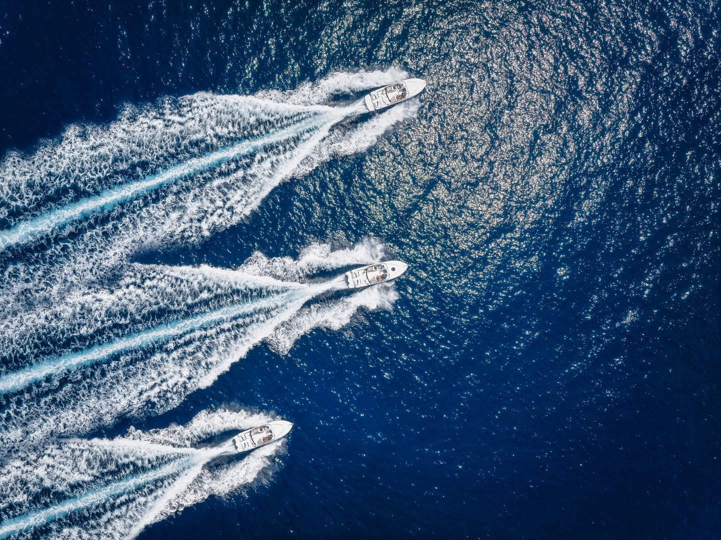 Aerial top down view of three motorboats cruising over the ocean with high speed