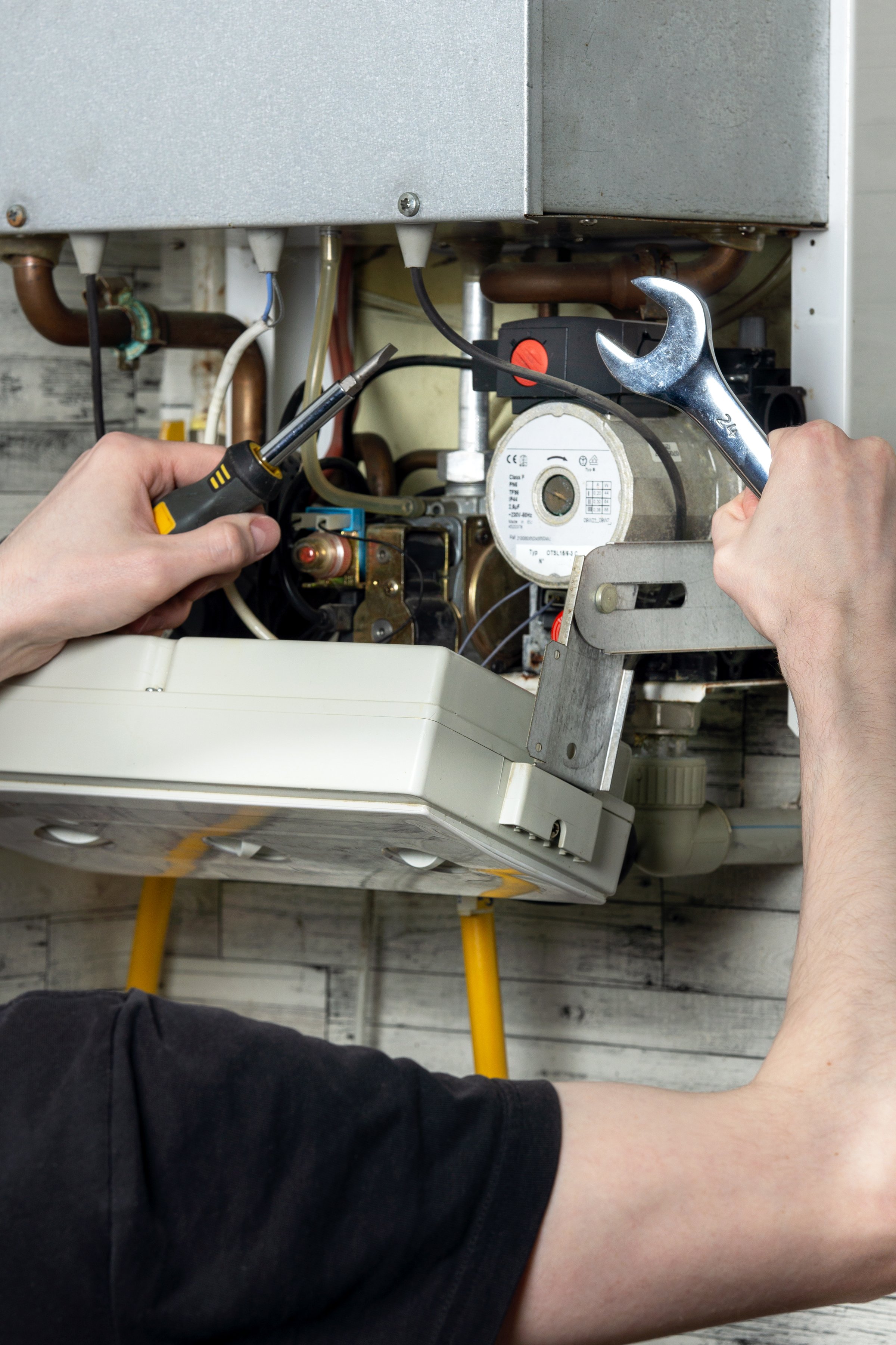 Maintenance of an electric water heating boiler; a man with a wrench and a spanner in his hands is repairing the boiler.