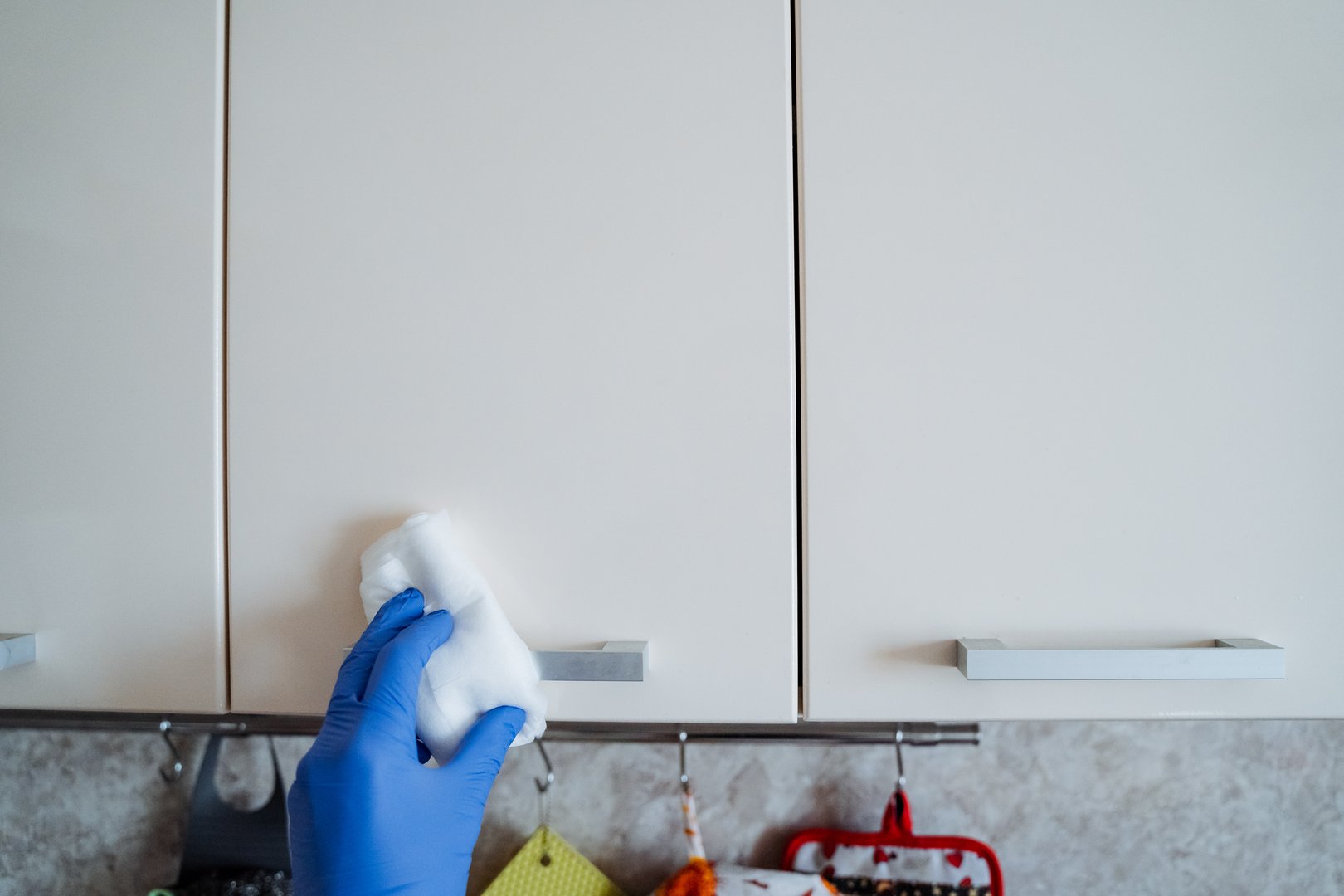 A person dressed in blue gloves is currently engaged in the careful and thorough cleaning of a kitchen cabinet with a cloth, meticulously ensuring that it is entirely spotless and hygienic for use