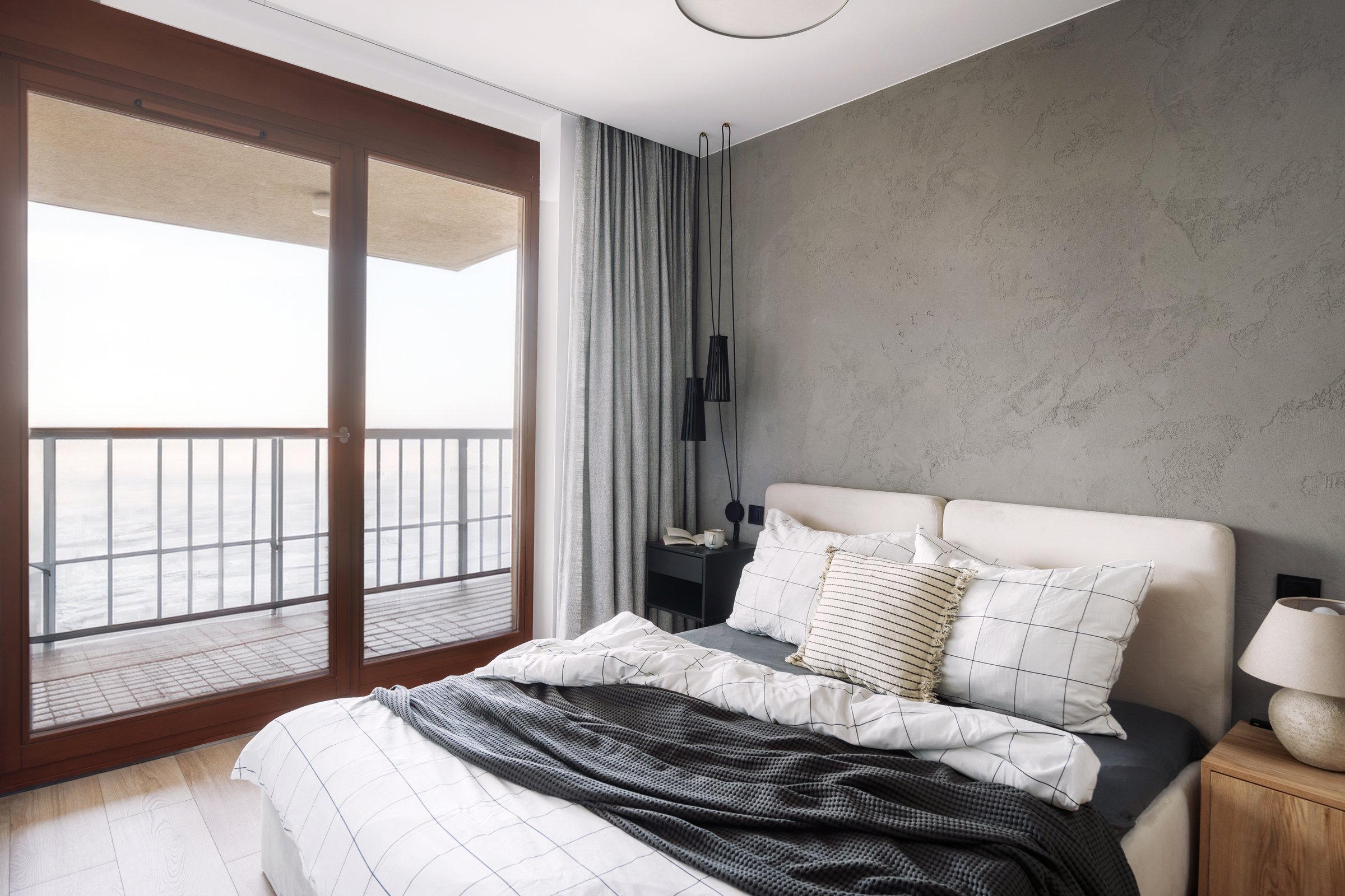 Cozy bedroom features a large bed with neutral bedding, stylish decor, and a balcony revealing a breathtaking ocean view during sunrise, creating a tranquil atmosphere.