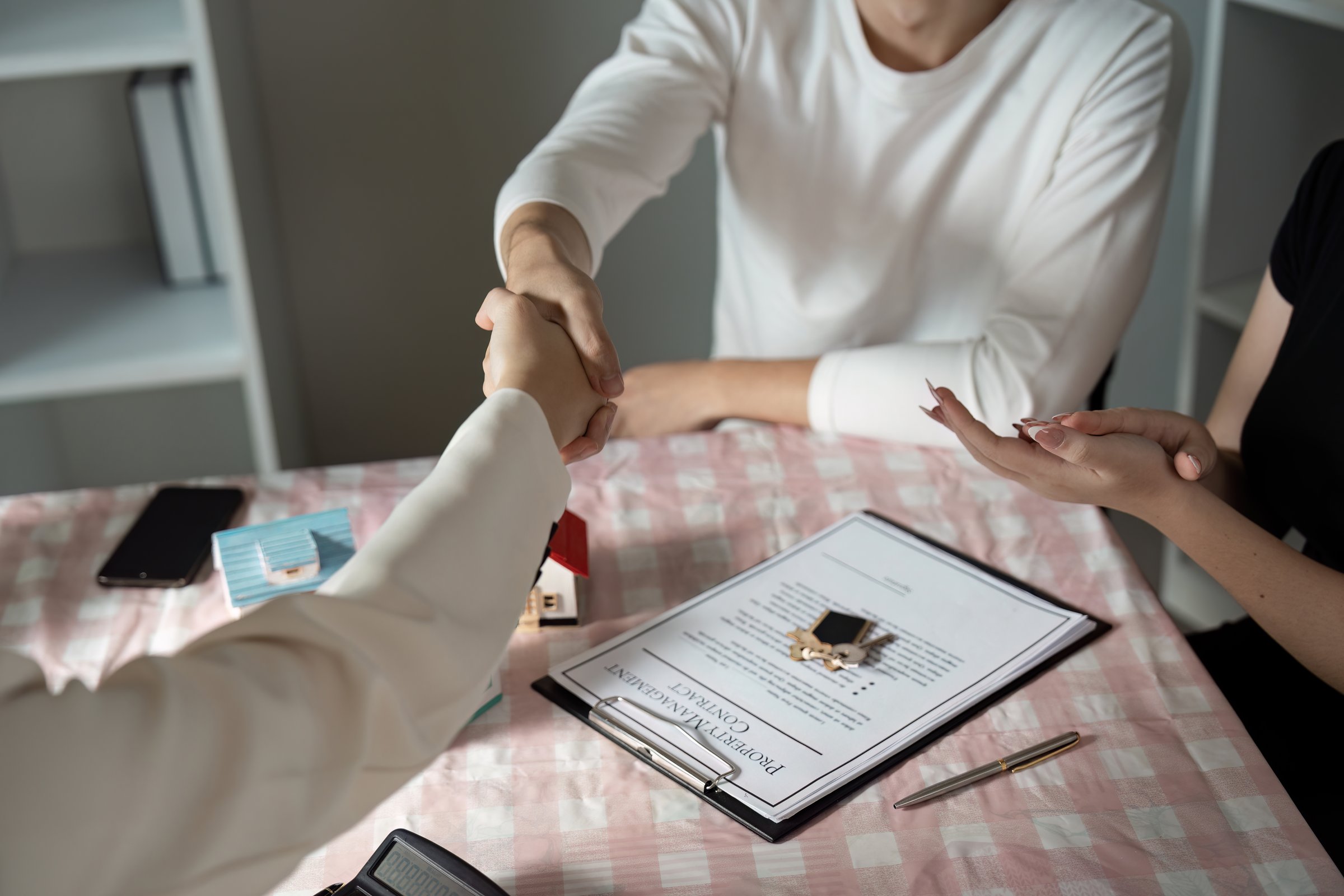 Real estate agent finalizing a property deal with clients, showcasing a contract and house model on a table.