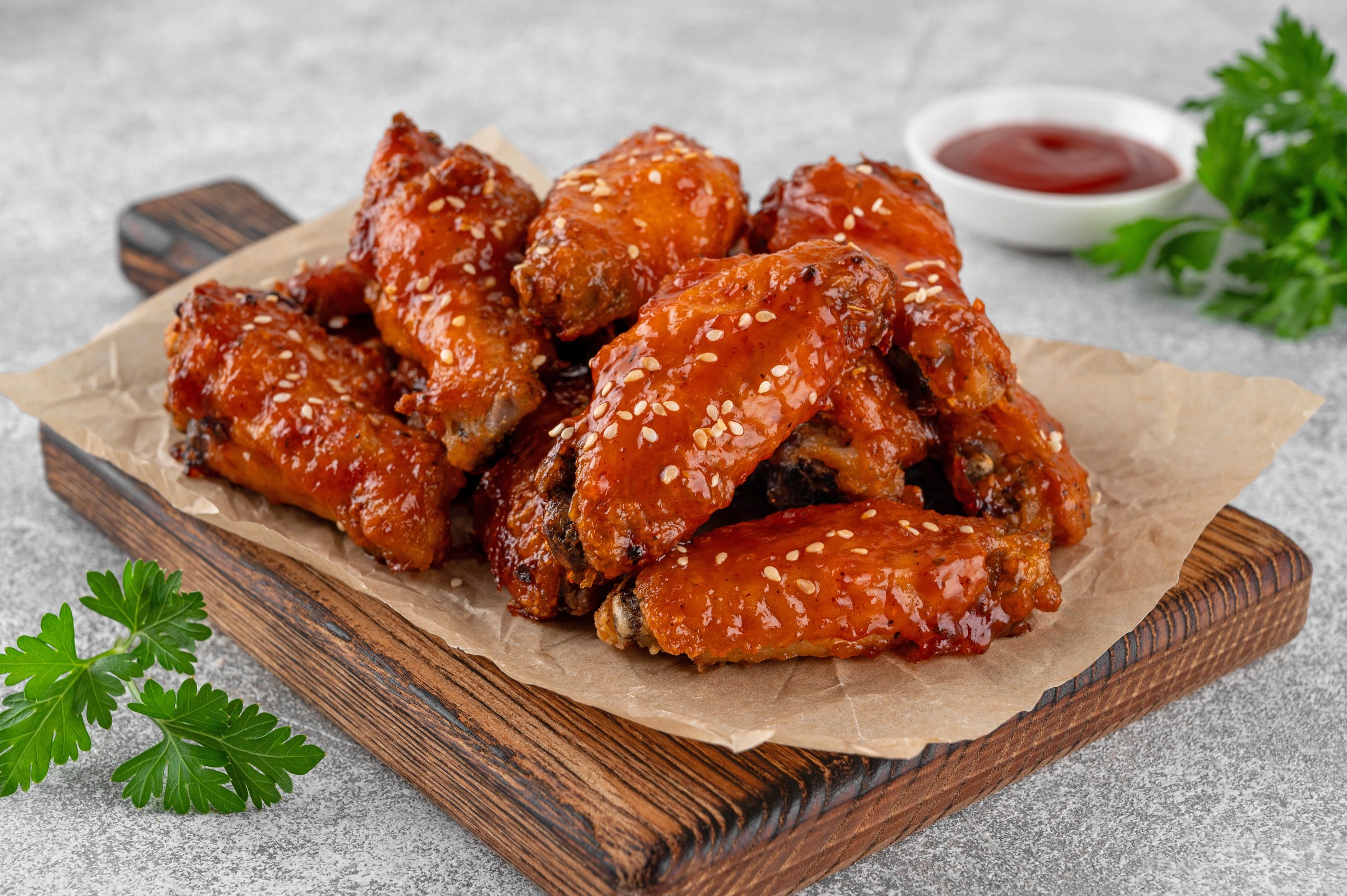 Baked chicken wings in a sweet chili sauce and sesame seeds on a wooden board on a concrete background. Close up