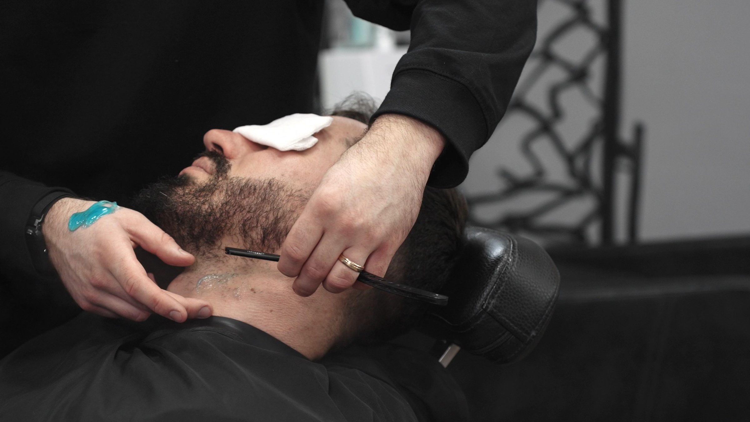 Professional barber shaving a client's beard with a straight razor, applying shaving gel and using a hot towel for a smooth and precise shave in a modern barbershop