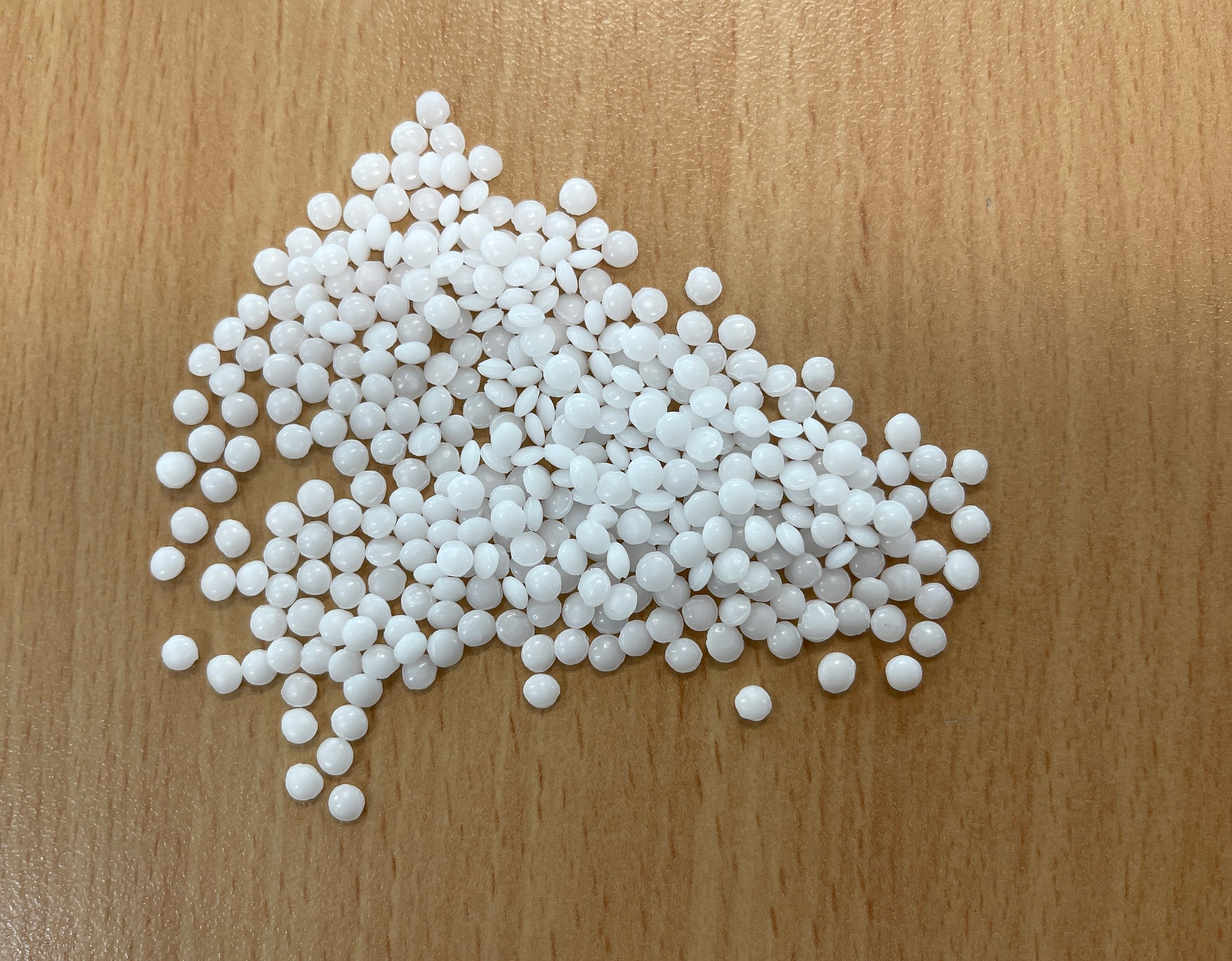 a pile of white pellets on a wooden table, production of plastic parts, plastic injection, a bunch of plastic pelets, plastic grains, horizontal