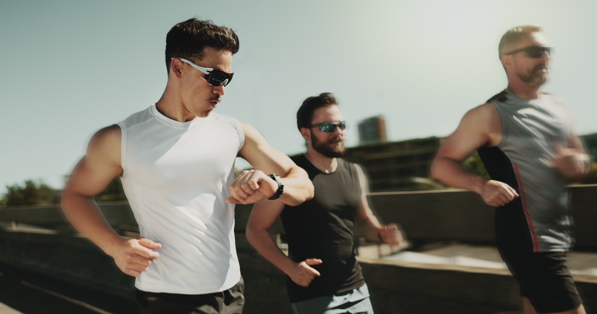 People, speed and running in city with watch, fitness tracker and check heart rate in urban town. Men, friends support and team blur for movement on street, outdoor cardio and monitor stats or timer