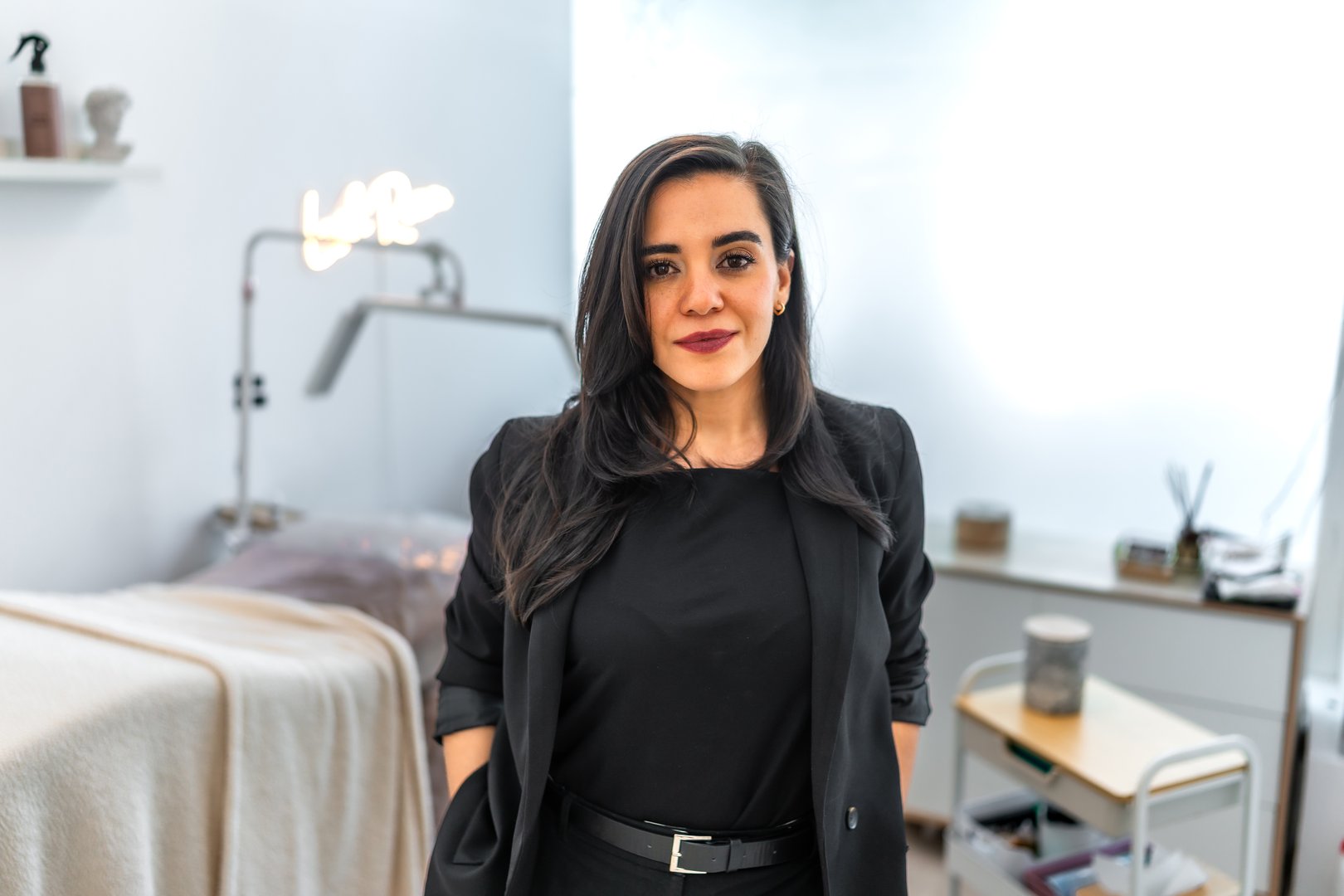 Portrait of a smiling young female beautician in a bright and modern beauty salon, exuding confidence while standing with hands in pockets