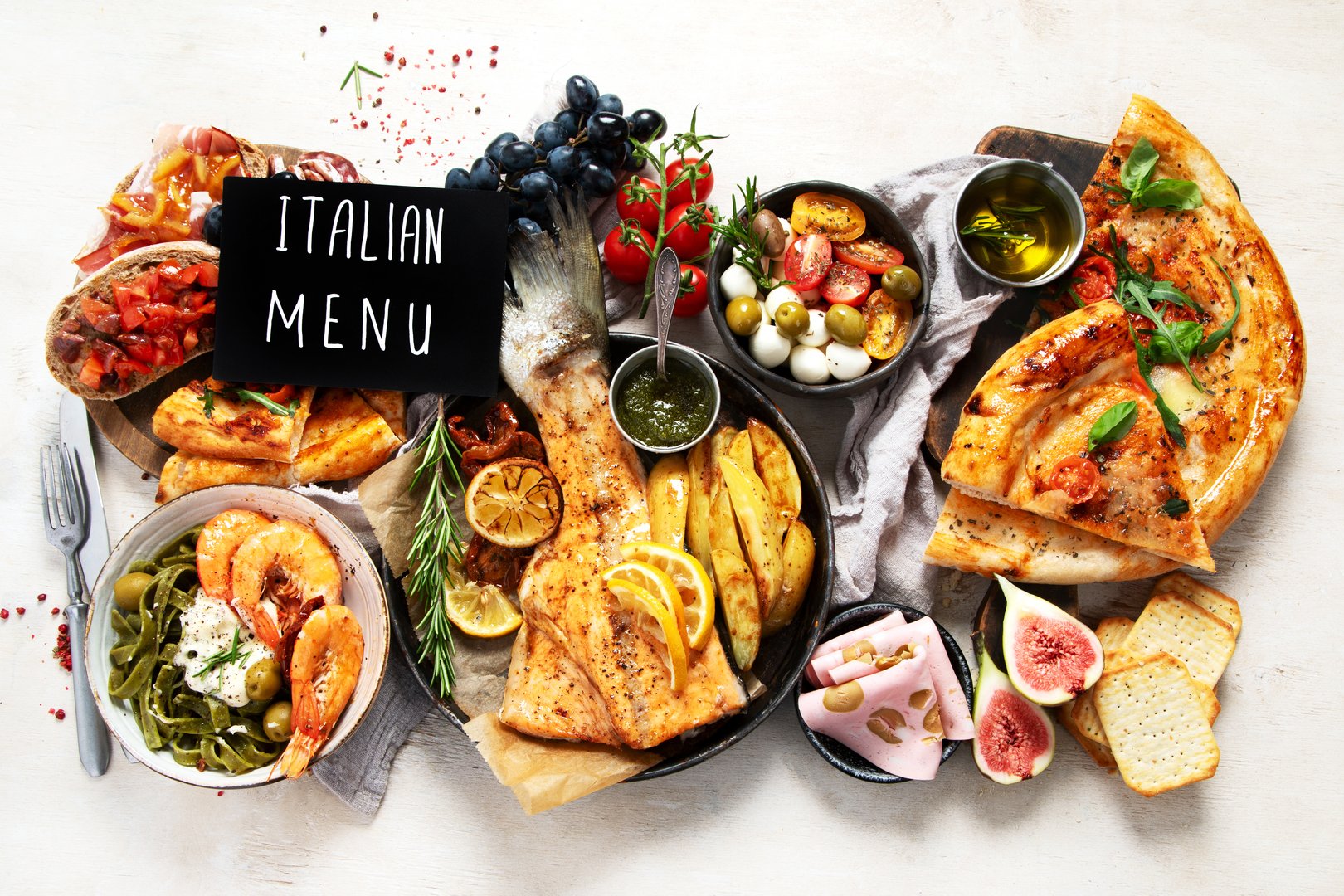 Full table of italian meals on plates and board - Pizza, pasta, salami, parmesan, olives, bread sticks on a white background. Top view.