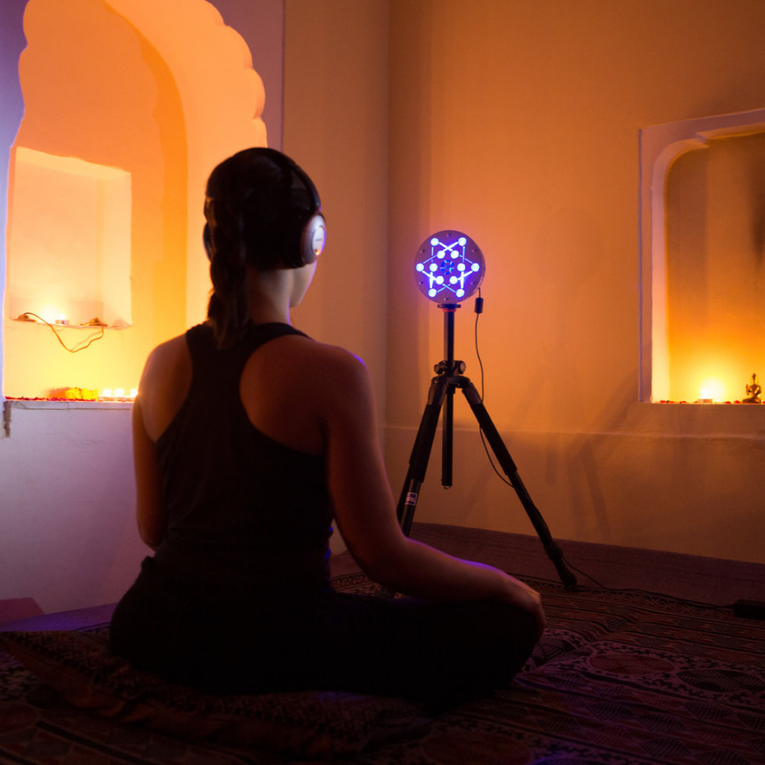Person meditating with headphones and lit sphere in dimly lit room, surrounded by candles and soft orange light.