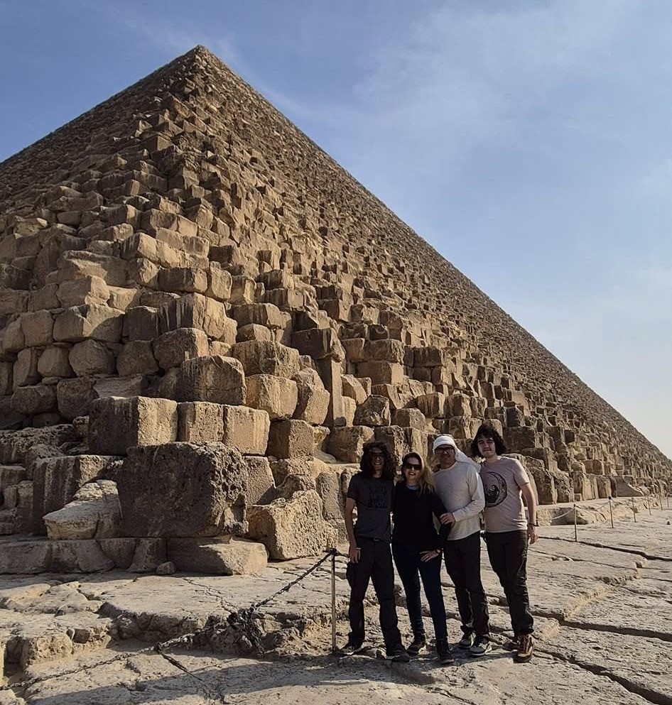 Four people standing in front of a large pyramid on a clear day.