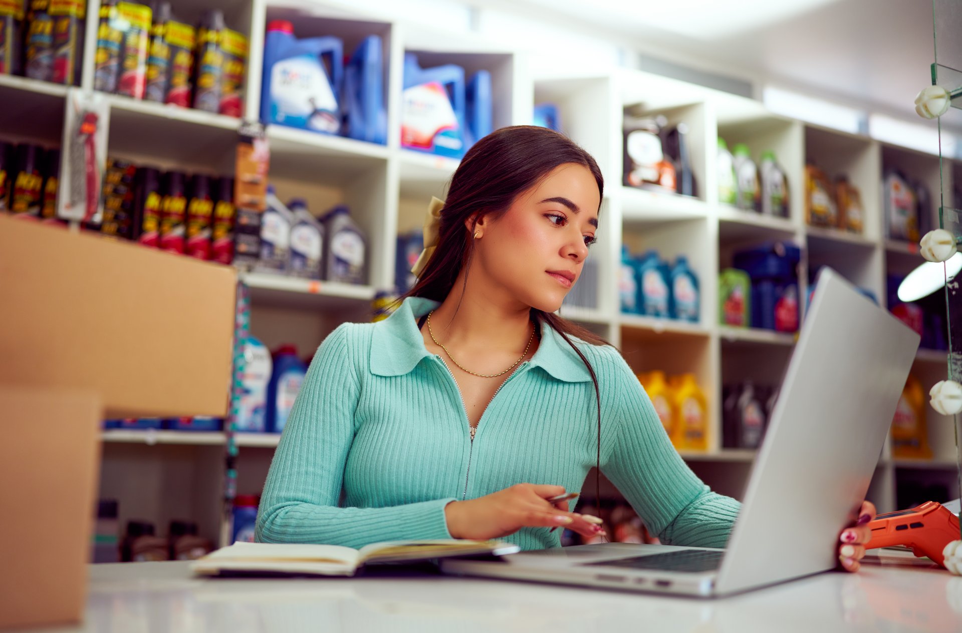 Young hispanic saleswoman using a laptop and taking notes in an auto parts store