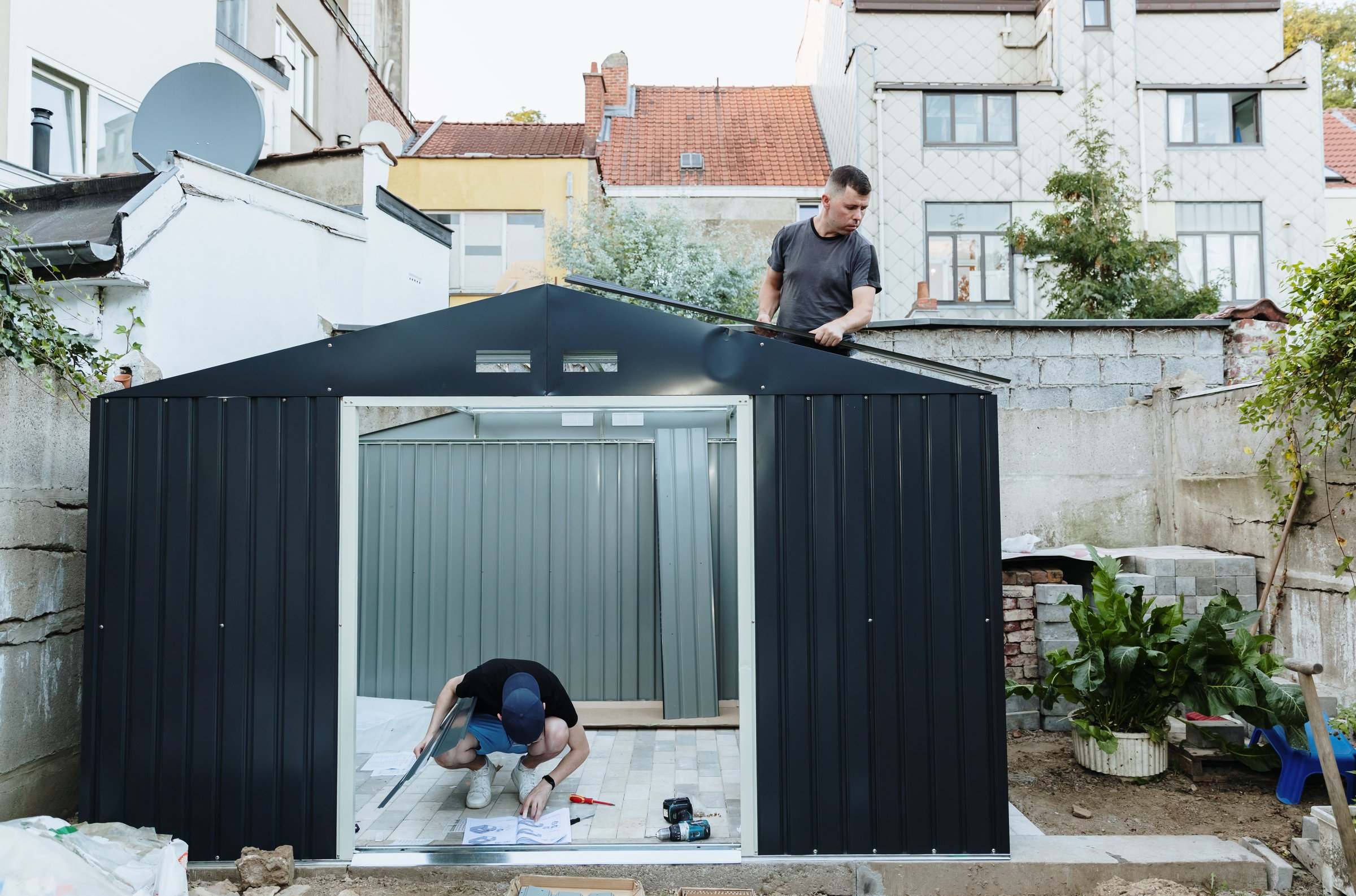 Portrait of two young workers installing steel roofing sheets on metal shed in backyard