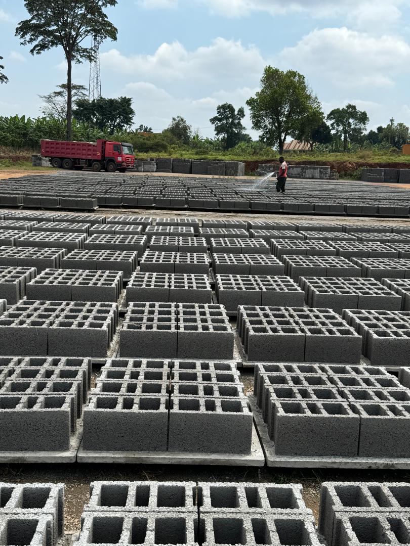 Concrete blocks drying outdoors in a large yard with a worker spraying water and a red truck in the background.