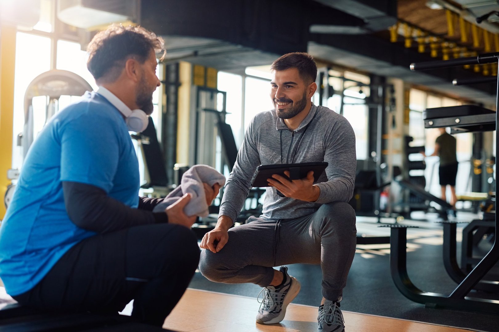 Young coach communicating with mature man while using digital tablet during sports training in health club.