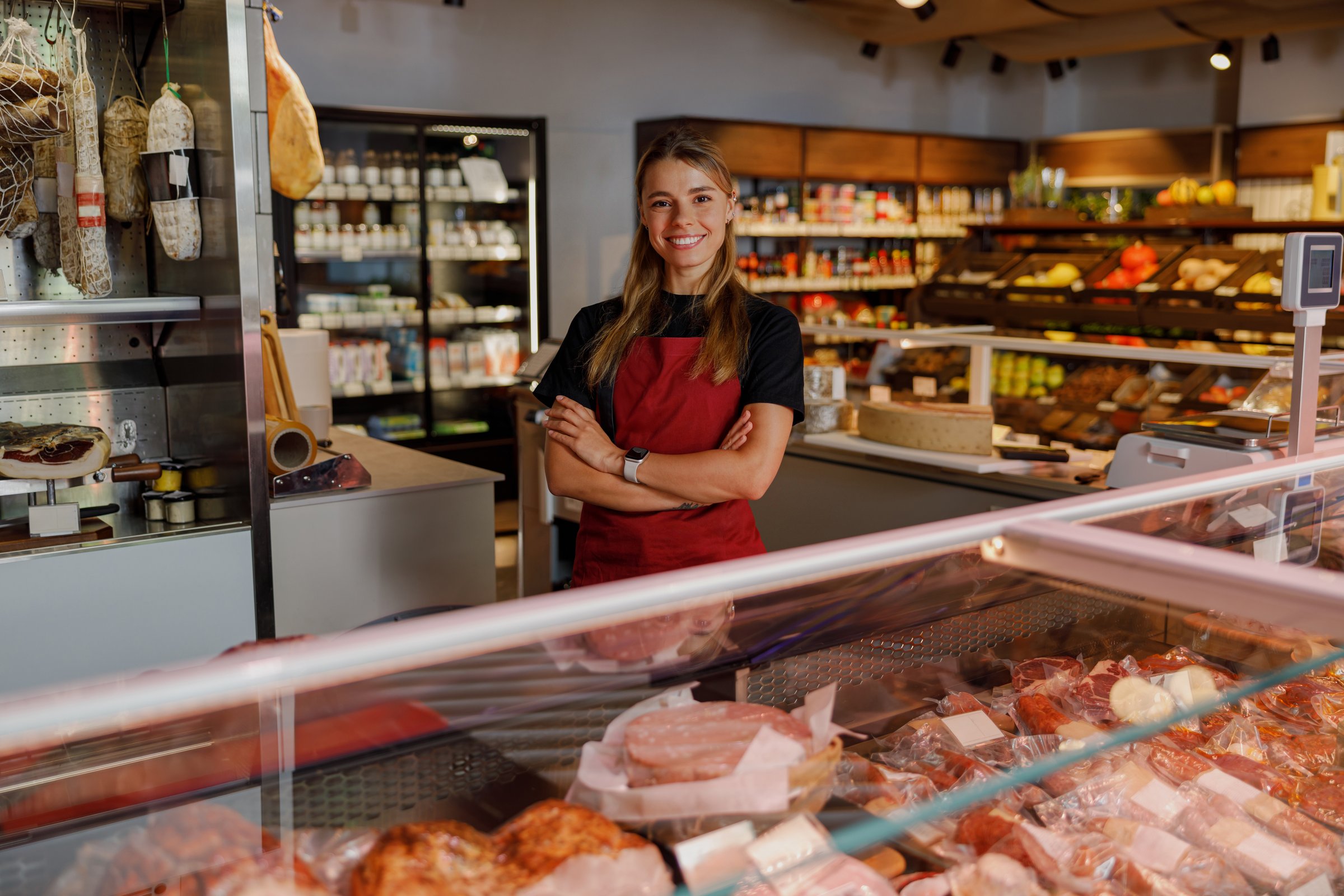 A confident and cheerful butcher smiles brightly in a wellstocked meat shop, proudly showcasing quality products