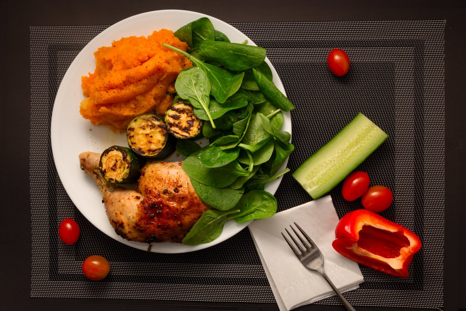Tasty fried chicken leg served with roasted zucchini, fresh spinach leaves, and a rich, orange-hued mashed potato and pumpkin mix.