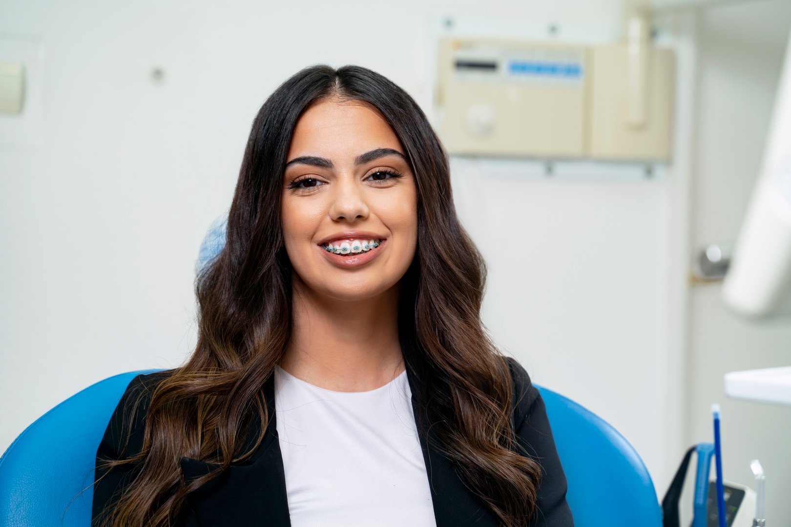 Elegant young adult woman sitting in dental chair, dental braces concept, looking at camera