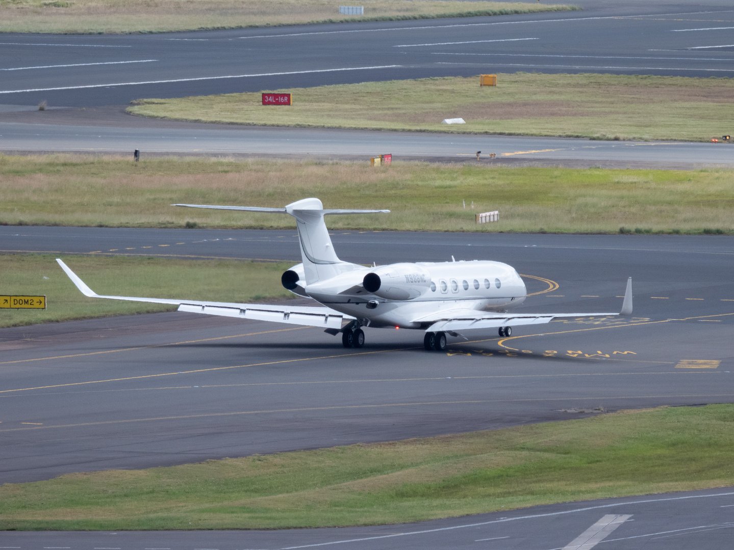A Gulfstream G650ER plane, registration N988NC, taxiing in preparation for departure from Sydney Kingsford Smith Airport and heading to Melbourne.  This image was taken from the 10th floor of a public carpark at the domestic terminal on a sunny and partly cloudy afternoon on 16 November 2024.