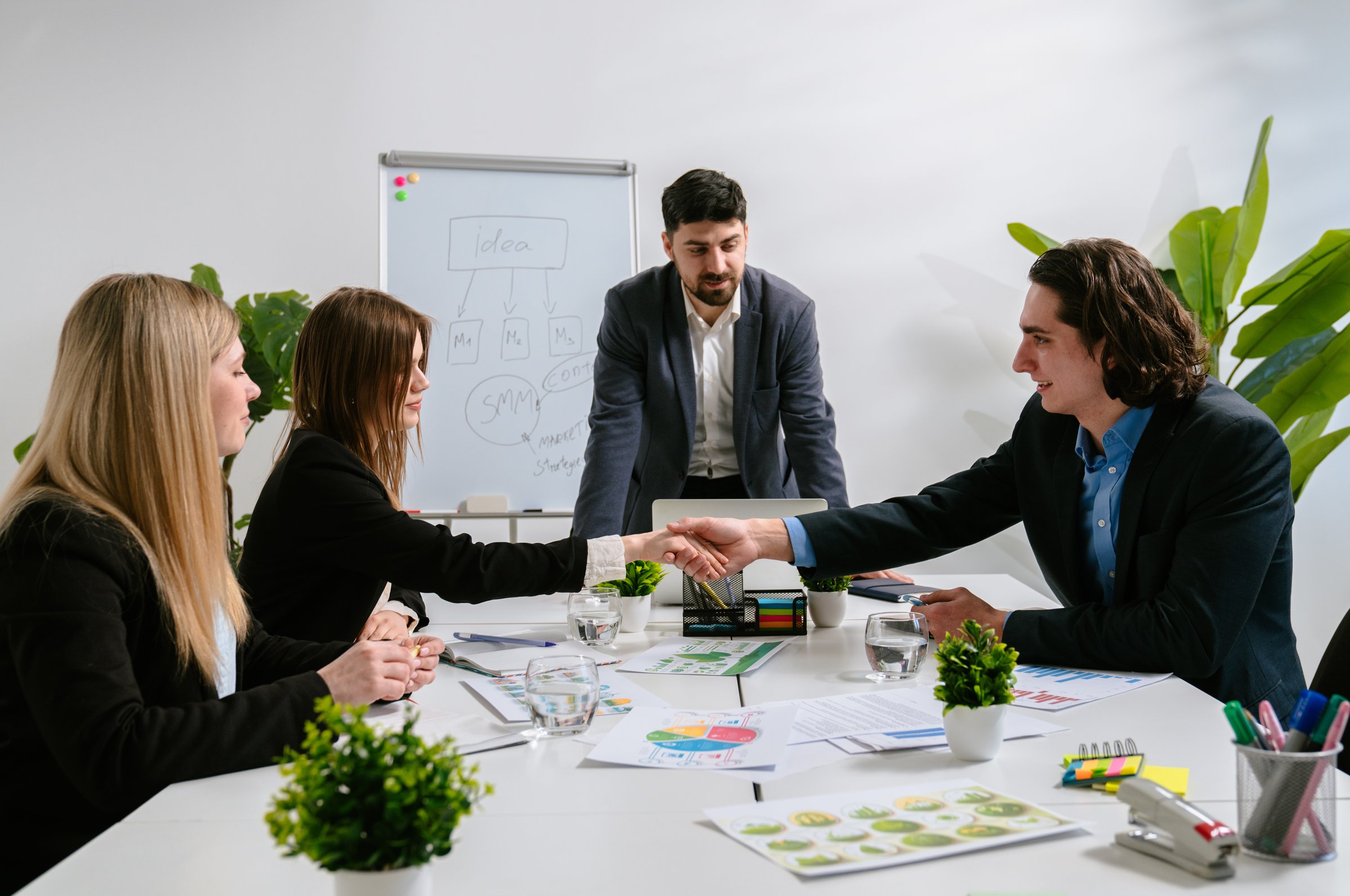 A team meeting in a modern office setting, with professionals discussing ideas and shaking hands.