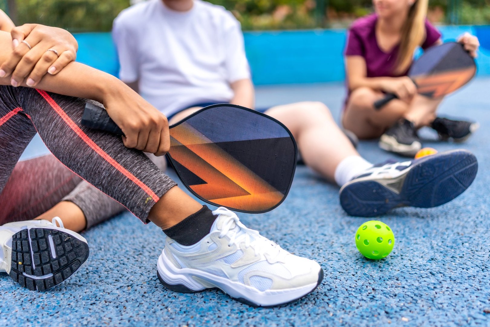 Cropped photo of an unrecognizable woman holding pickelball racket while talking with diverse friends