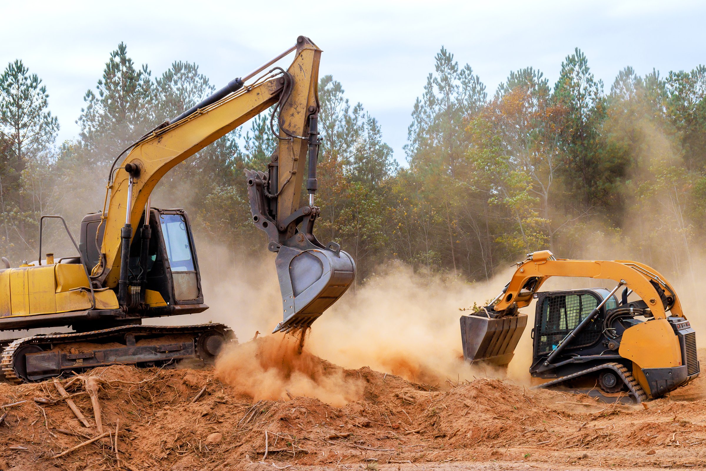 Bulldozer excavator heavy machinery work together to clear excavate land on construction site dust rises as they dig into ground, preparing for upcoming development.