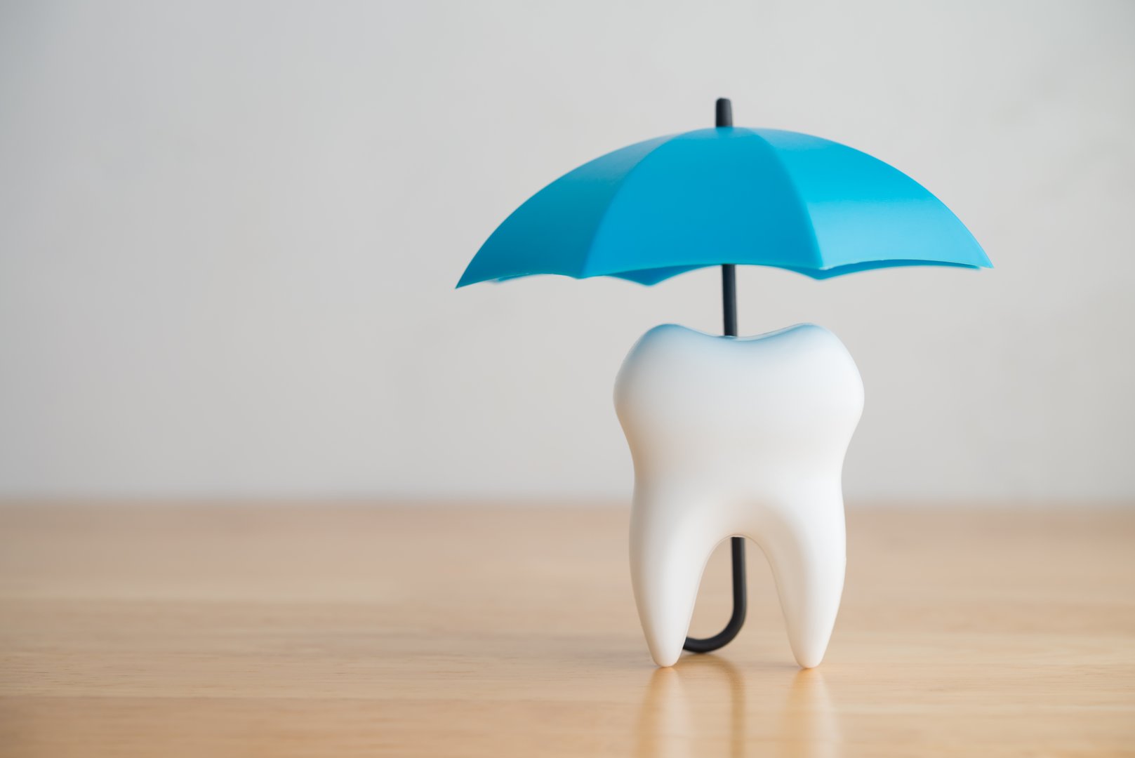 Blue umbrella covers white clean tooth on white background copy space. Dental insurance, dental care, tooth protection concept. Dental health insurance is a contract that helps pay for dental care costs