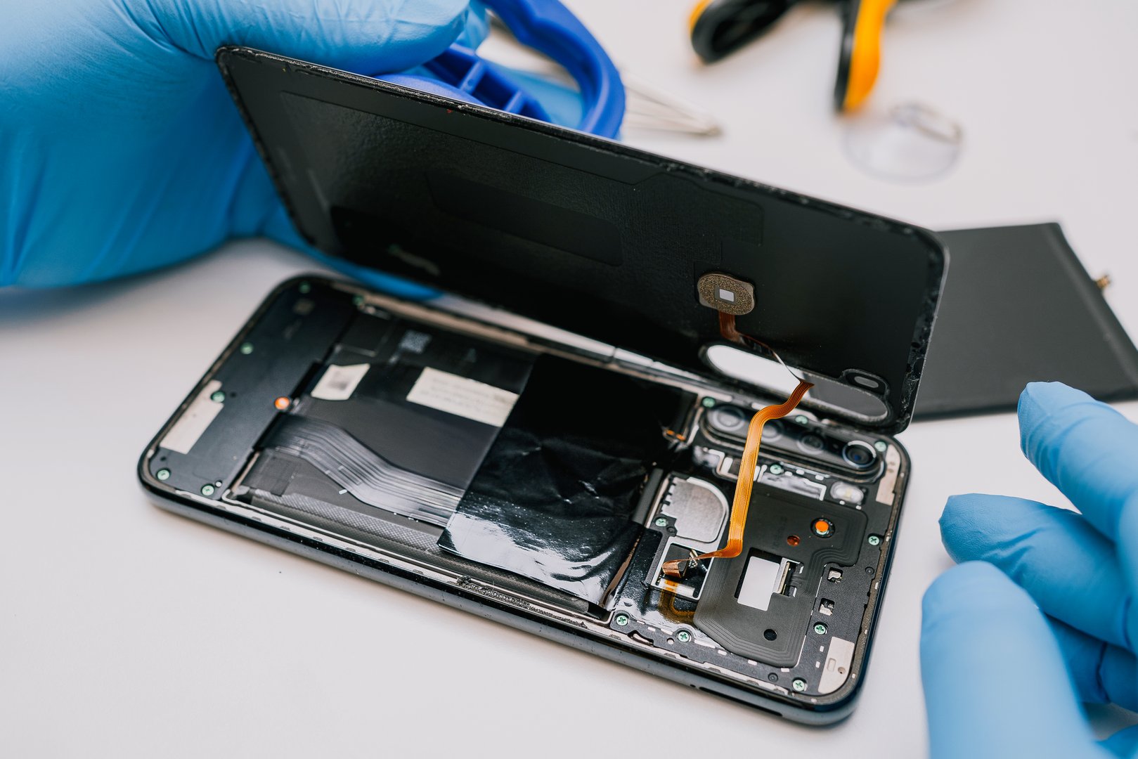 Battery replacement in a mobile phone â a technician in protective gloves disassembles a smartphone, removing the back cover to install a new battery. Repair and maintenance process of electronics.