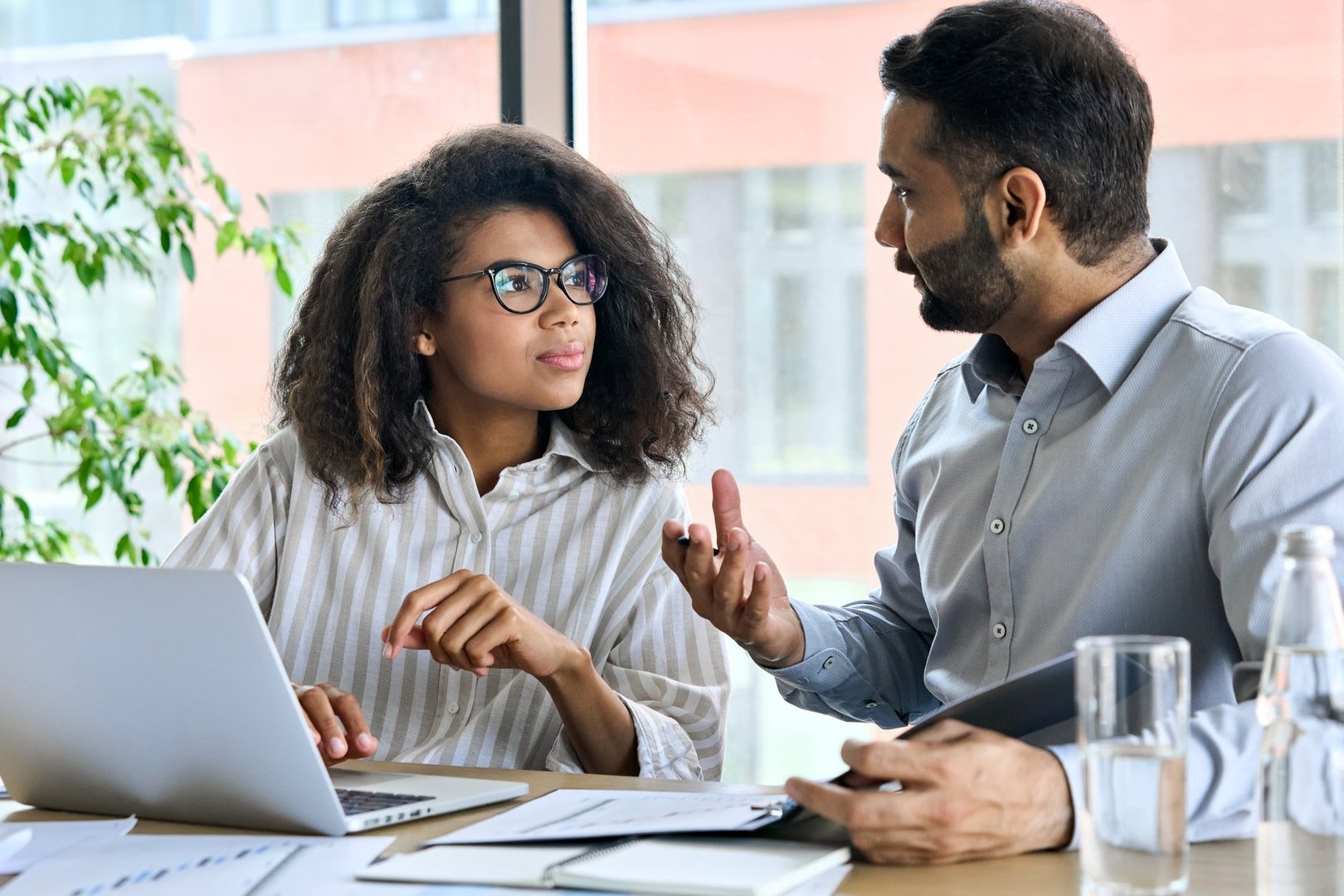 Businessman indian executive manager ceo talking to female African American coworker, using laptop. Diverse multicultural professional partners group discussing business plan at board room meeting.
