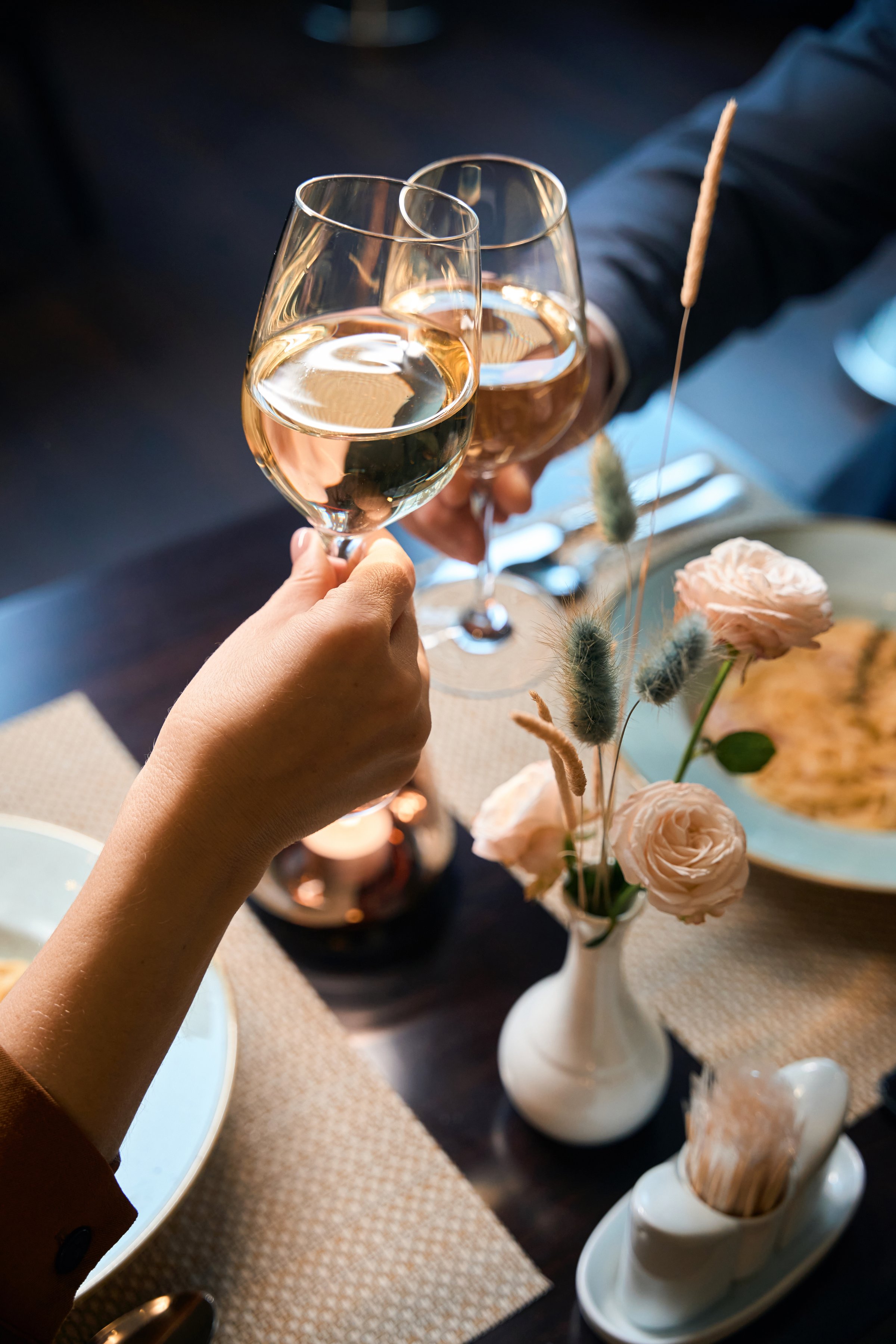 Partial image of couple toasting wine from glasses at table in hotel restaurant. Concept of romantic date and event