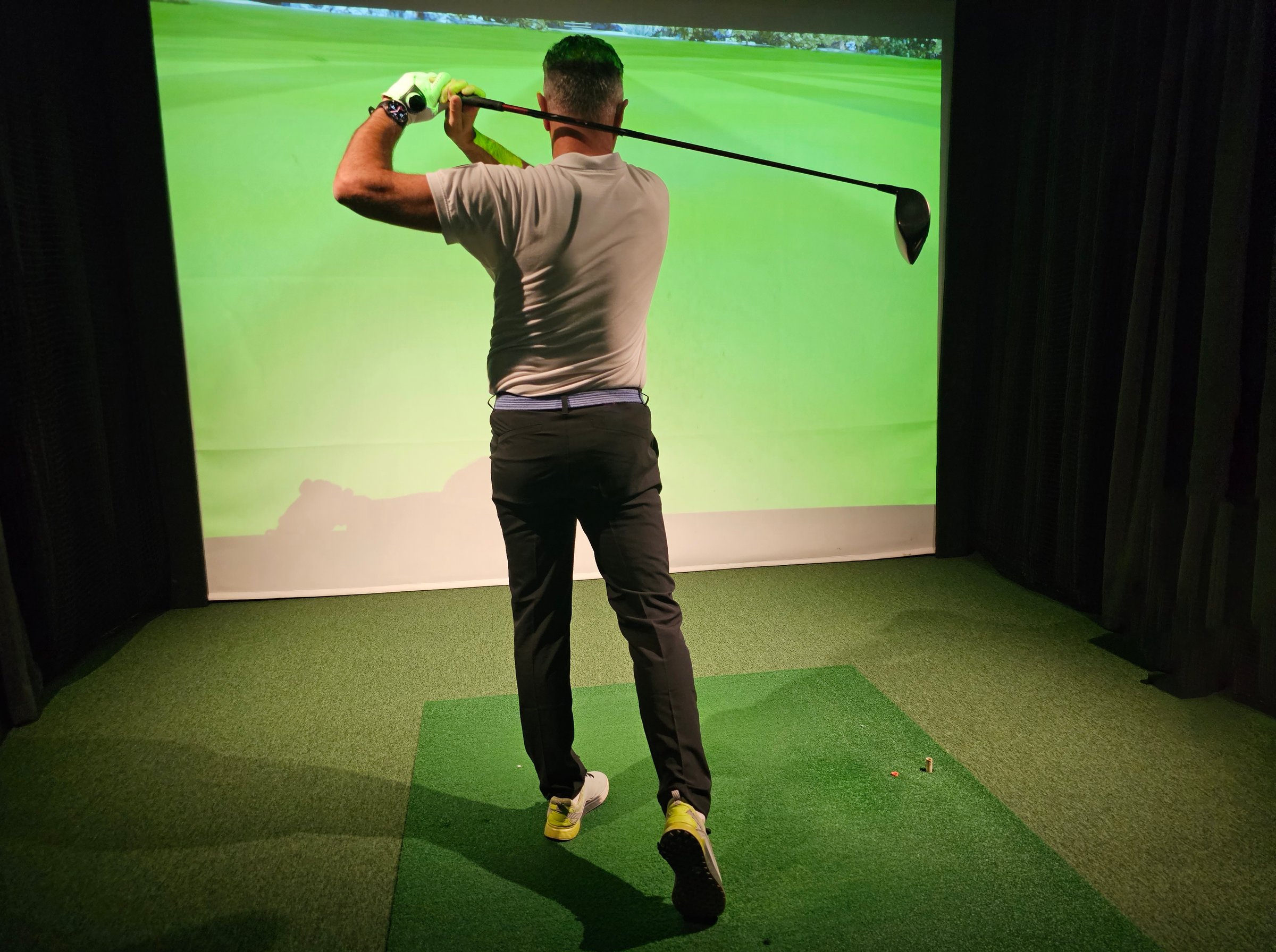 Professional male golfer holding club playing golf indoors on golf simulator