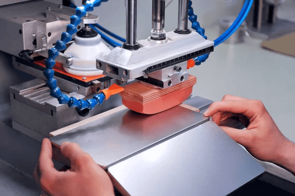 Pad printing machine applying ink on an object. Hands position the item under the machine head.