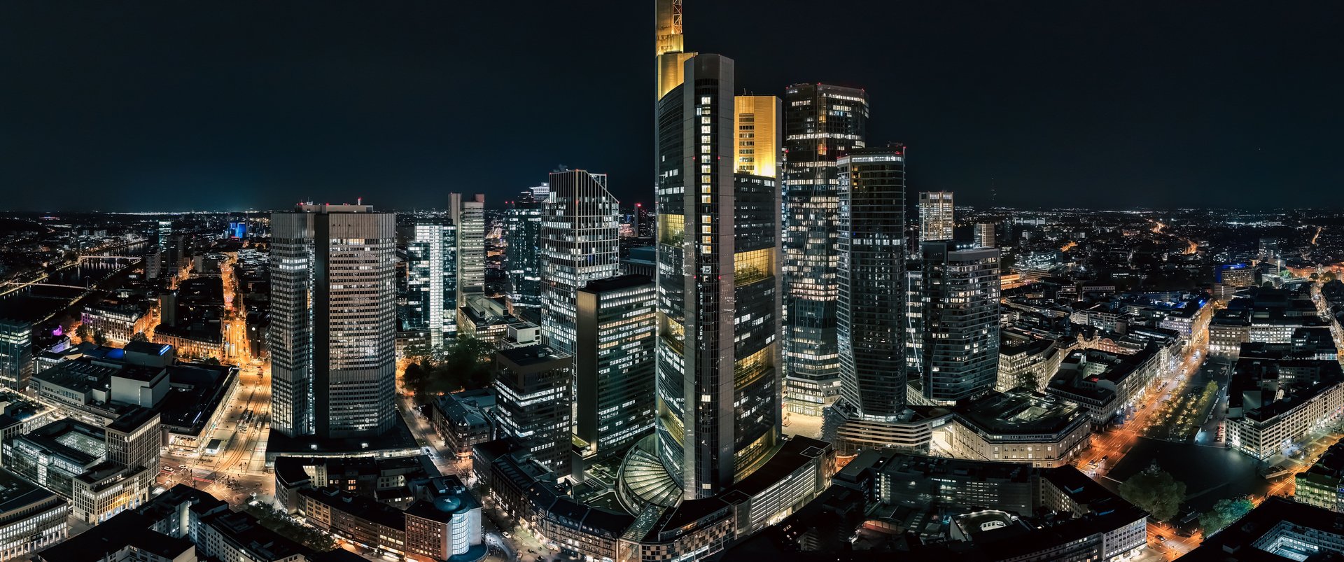 Panoramic night view of Frankfurt's illuminated skyline featuring modern skyscrapers and city lights.