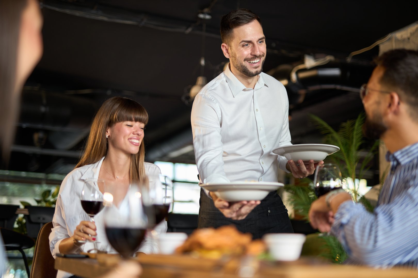 Freundlicher Kellner serviert Geschäftsleuten während Mittagszeit im Restaurant - Symbolbild für professionellen Kellner-Service und erstklassige Gästebetreuung