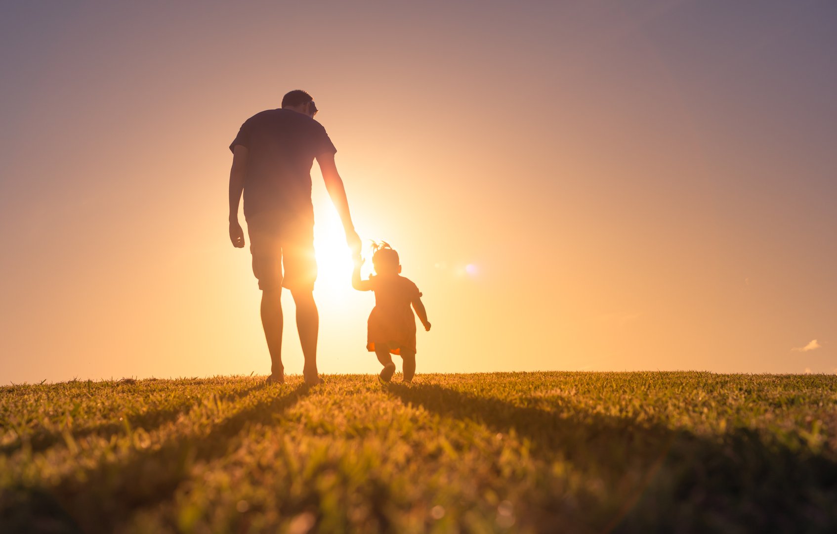 Father and daughter walking at sunset outdoors.