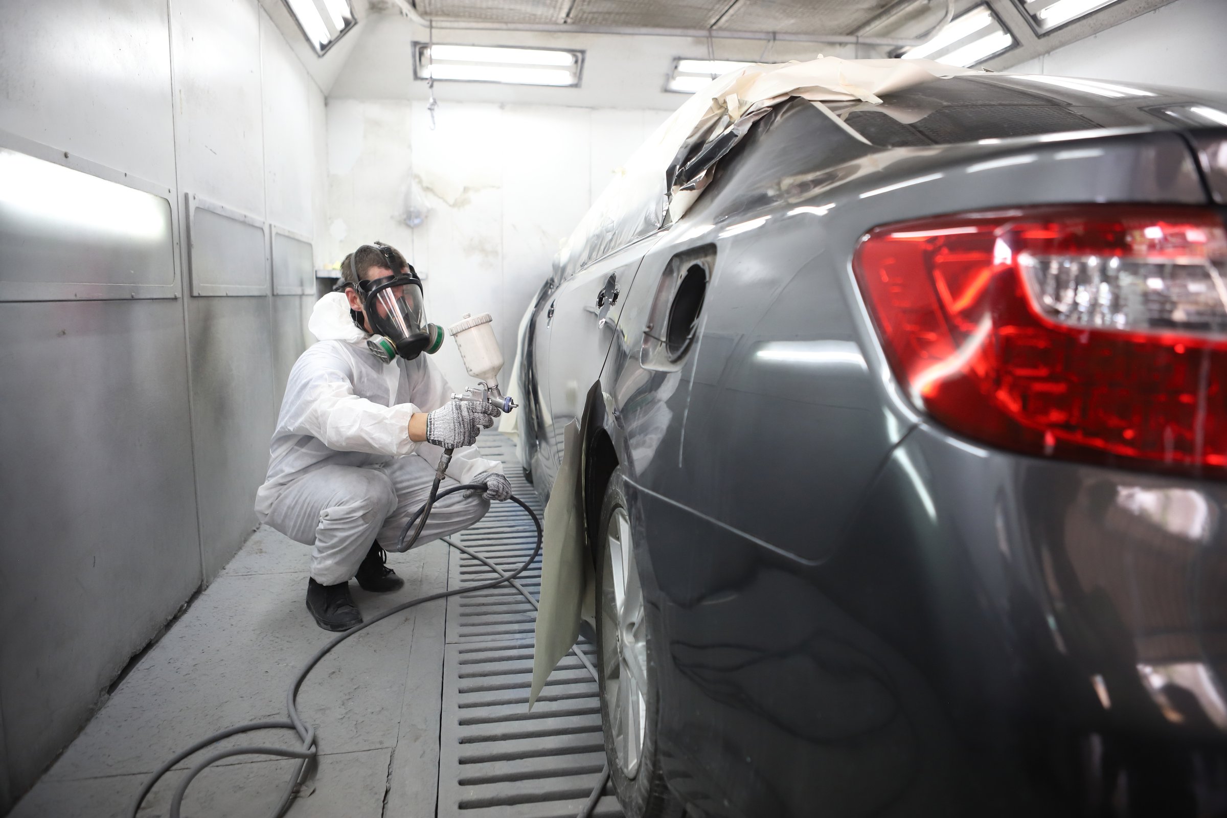 auto mechanic worker painting, automobile repairman painter in protective workwear and respirator painting car body in paint chamber