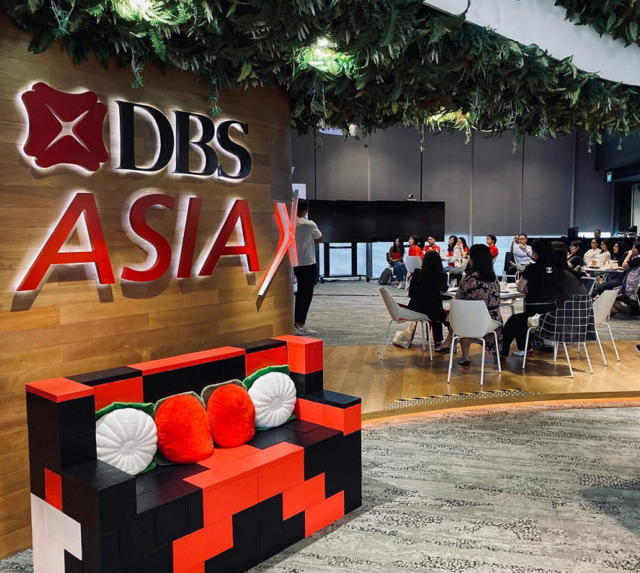 Interior of DBS Asia office with a branded wall, red sofa, and people sitting in a meeting area.